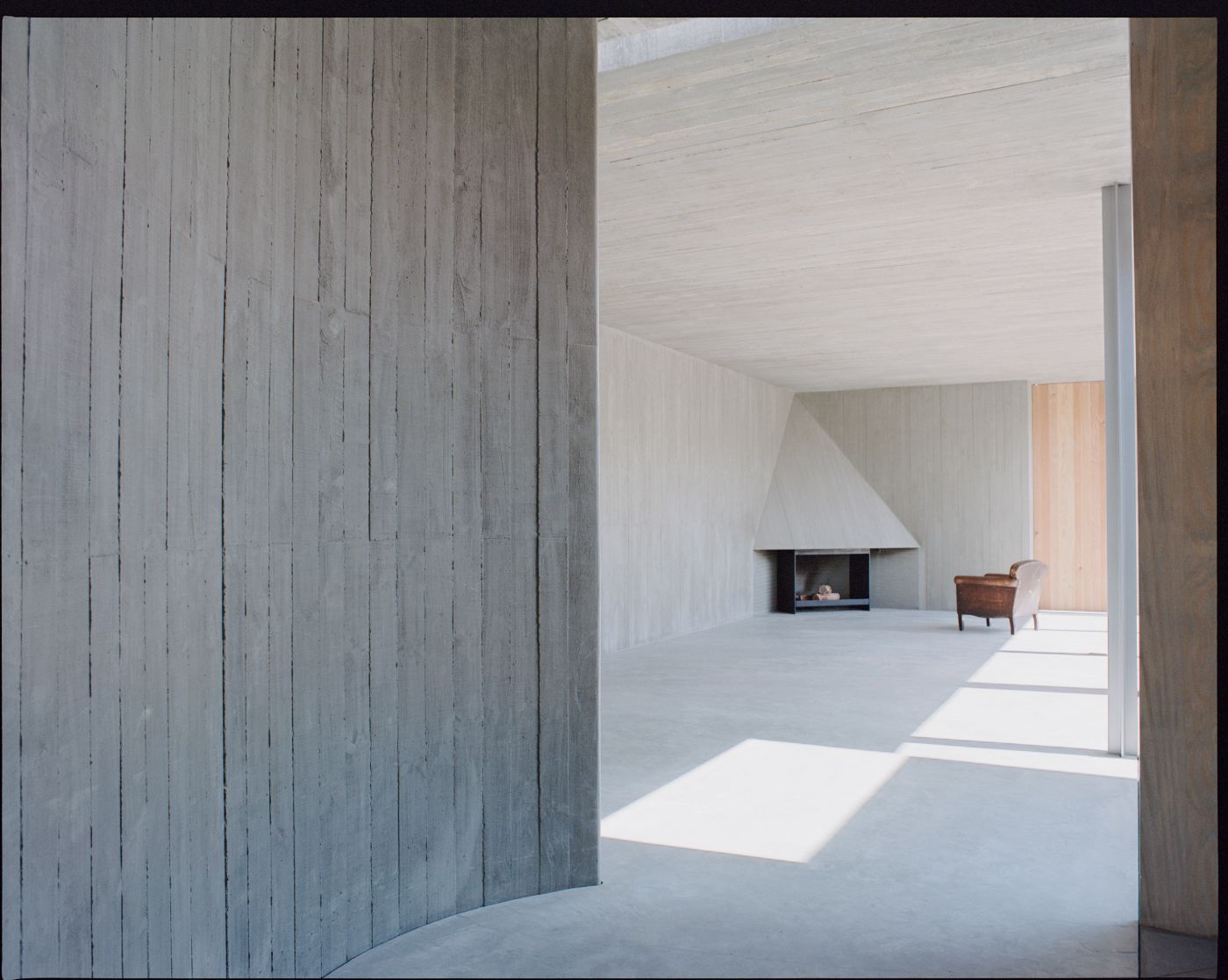 Mori House by Aires Mateus + MAArchitects — A passage through whitewashed vertical timber walls frames a generous interior volume bathed in rectangular light.