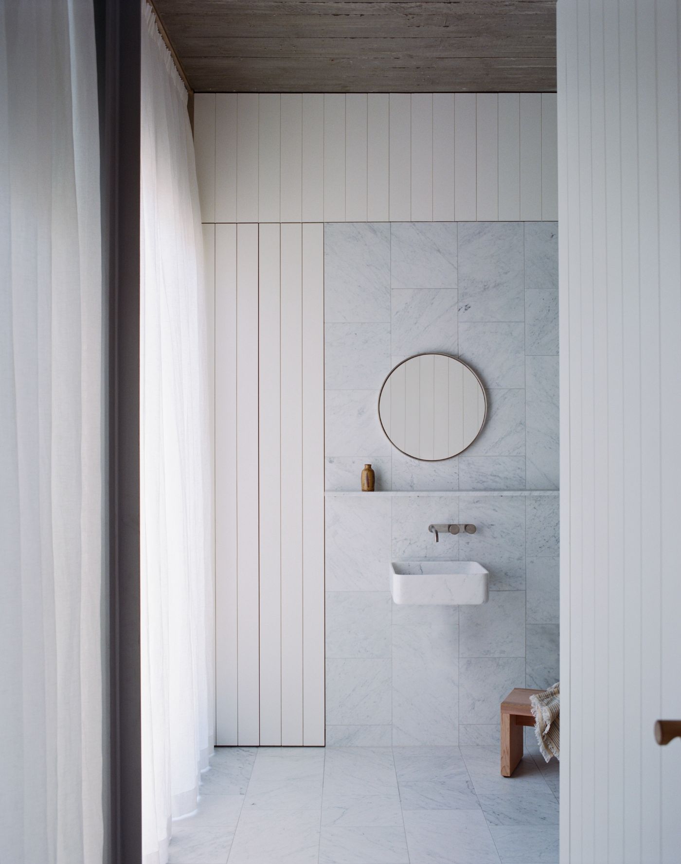 Mori House by Aires Mateus + MAArchitects — A minimalist bathroom interior dominated by marble tile cladding in soft grey-white tones.