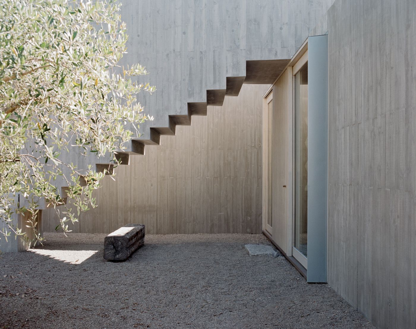 Mori House by Aires Mateus + MAArchitects — A courtyard passage framed by monolithic concrete walls with vertical timber cladding in cream tones.