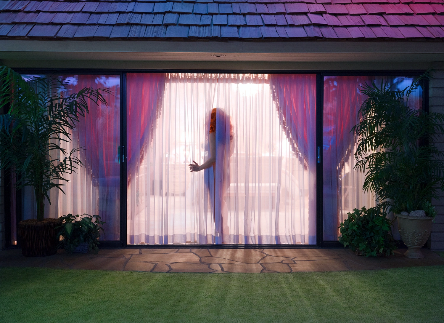 What to do with a Million Years by Juno Calypso — A silhouetted figure stands before floor-to-ceiling glass doors framed by gathered mauve fabric valances with theatrical proportions.