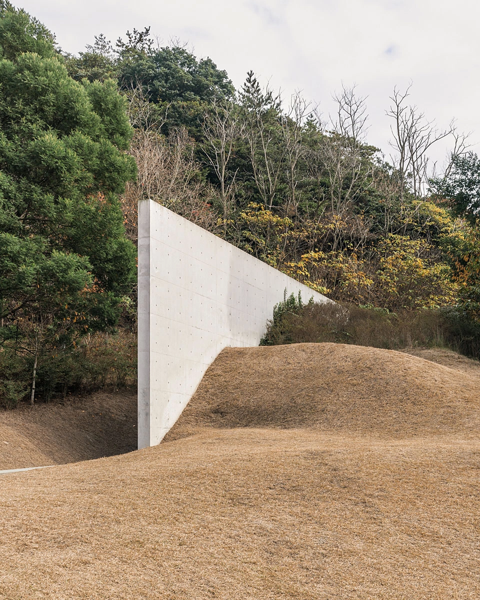 Lee Ufan Museum by Tadao Ando captured by Dan Preston — A monolithic concrete wall angles sharply against an earthen slope, its angled plane meeting bare ground at an acute geometric intersection.
