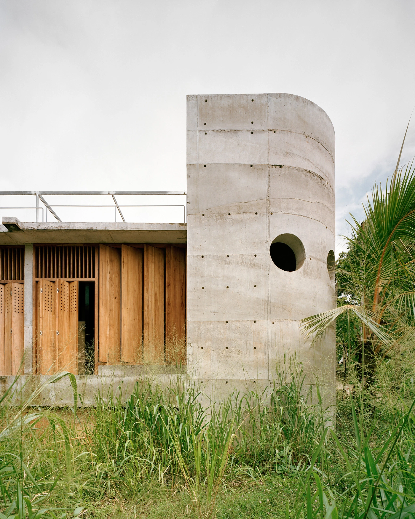 057 Guesthouse Hiriketiya by Atelier Abraha Achermann — A cast concrete cylindrical tower dominates the composition, its monolithic form marked by horizontal board-formed striations and regular grid of formwork...