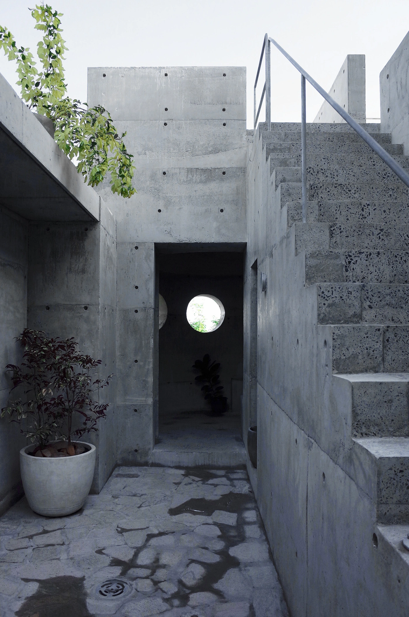 057 Guesthouse Hiriketiya by Atelier Abraha Achermann — A narrow concrete passageway frames a circular void punched through the far wall, creating a luminous focal point that draws the eye through the compressed...