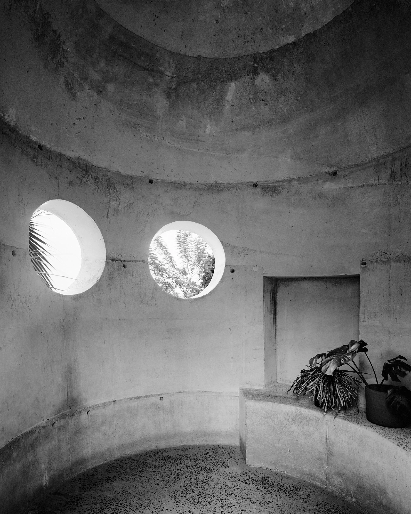 057 Guesthouse Hiriketiya by Atelier Abraha Achermann — A monolithic concrete cylindrical interior punctuated by two circular voids that frame views of tropical vegetation and sky.