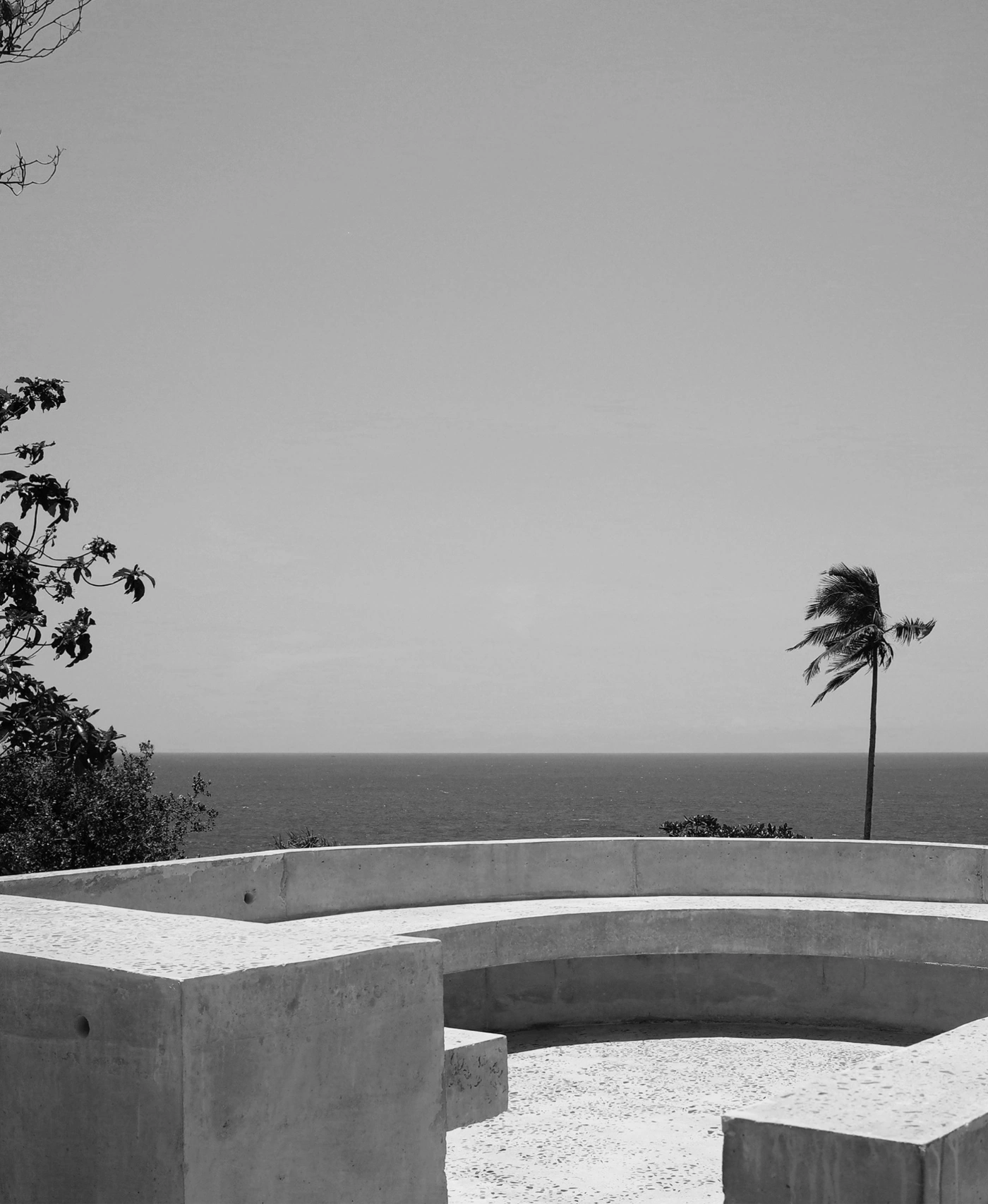 057 Guesthouse Hiriketiya by Atelier Abraha Achermann — Monolithic concrete seating elements with curved geometry define a raised coastal platform overlooking the Indian Ocean.