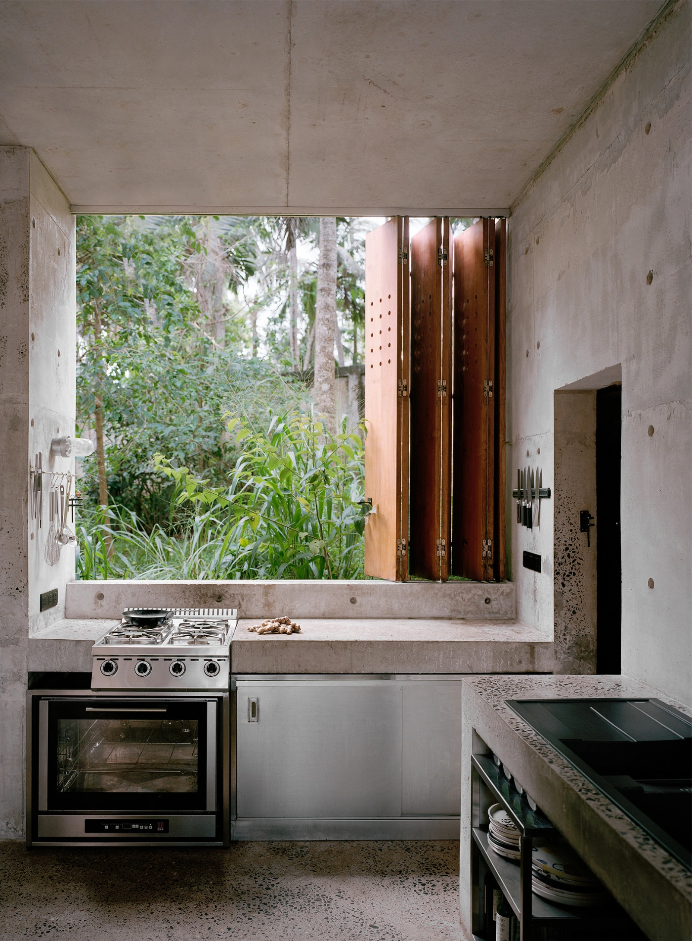 057 Guesthouse Hiriketiya by Atelier Abraha Achermann — A monolithic concrete kitchen set into a deep recessed window opening frames lush tropical vegetation and tall palms.