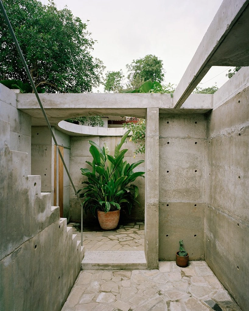 057 Guesthouse Hiriketiya by Atelier Abraha Achermann — A monolithic cast-concrete passage frames a lush potted plant in the interior courtyard beyond.