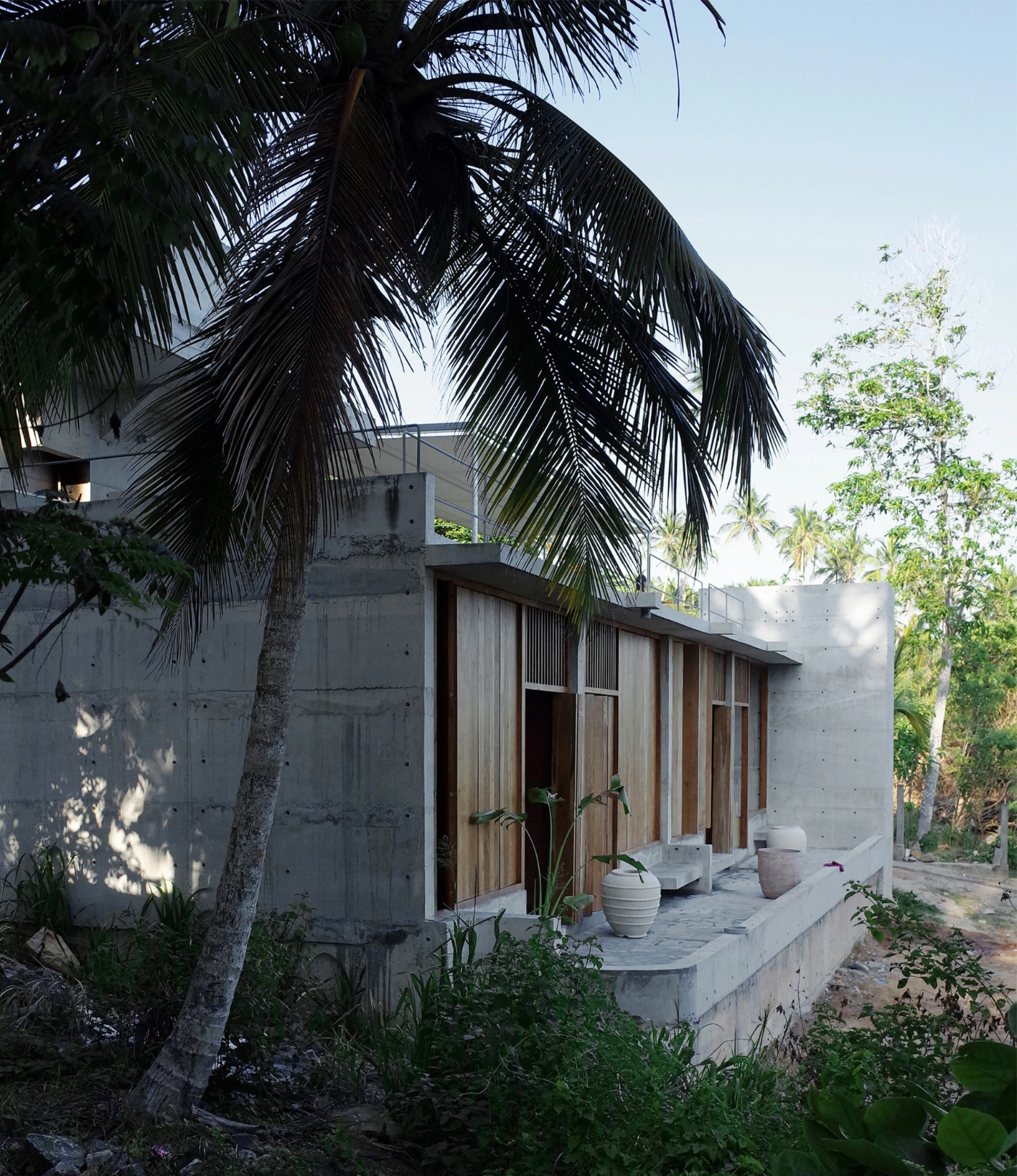 057 Guesthouse Hiriketiya by Atelier Abraha Achermann — A board-formed concrete guest room structure frames the photograph, its raw cylindrical tower punctuated by two circular voids at staggered heights.