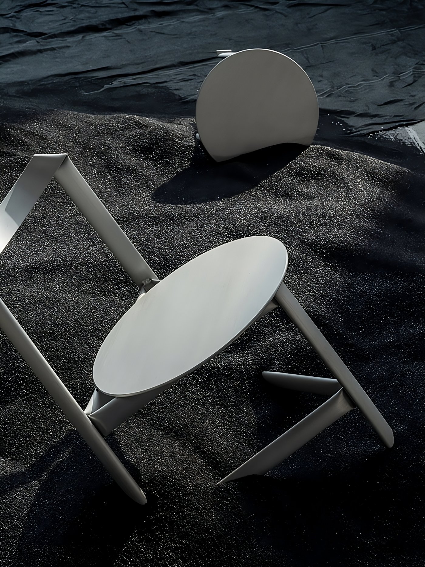 MONOCHROME by Ximi Li — Three aluminum furniture objects arranged on a dark granular surface.