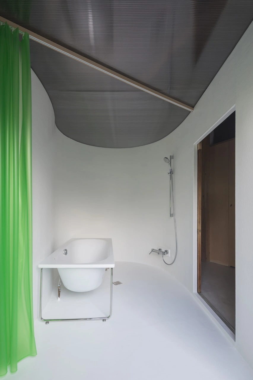 House in Kamisawa by Tato Architects — A compact bathroom module designed with a curved polycarbonate ceiling vault that descends organically into the white plaster-lined space.