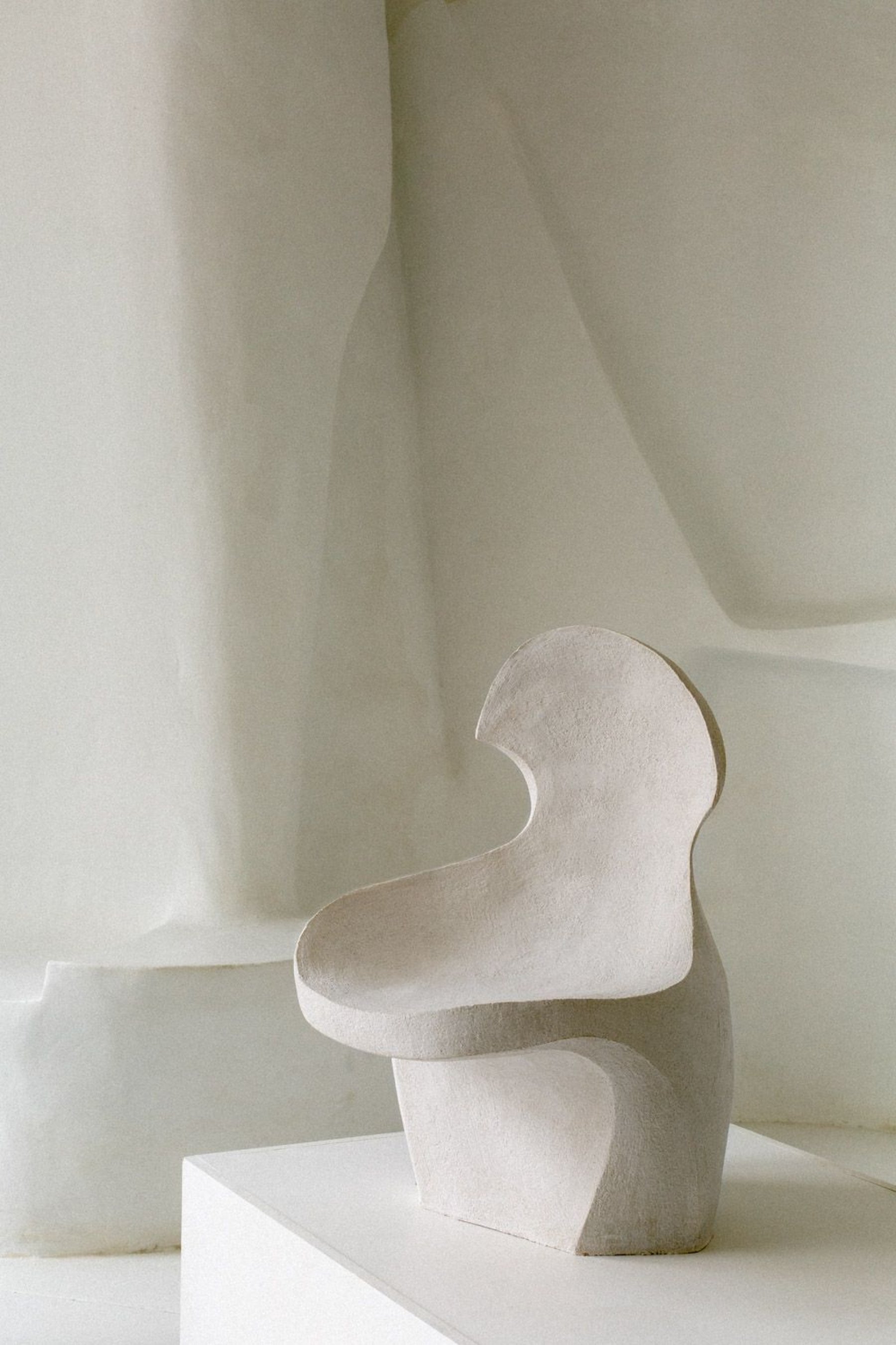 Selected works by Simone Bodmer-Turner — A sculptural ceramic form in off-white matte finish sits on a white plinth against a monochromatic gallery wall.