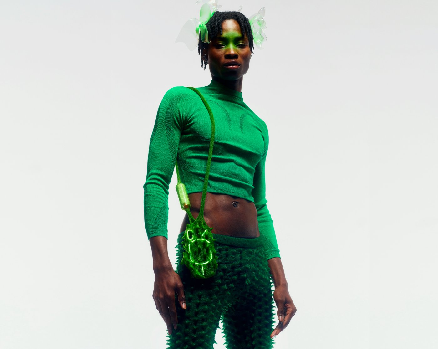 Nothing x Chet Lo — A figure wears a cropped fitted knit top in neon green with visible seaming detail, paired with textured knit pants featuring raised spike or scale-like...