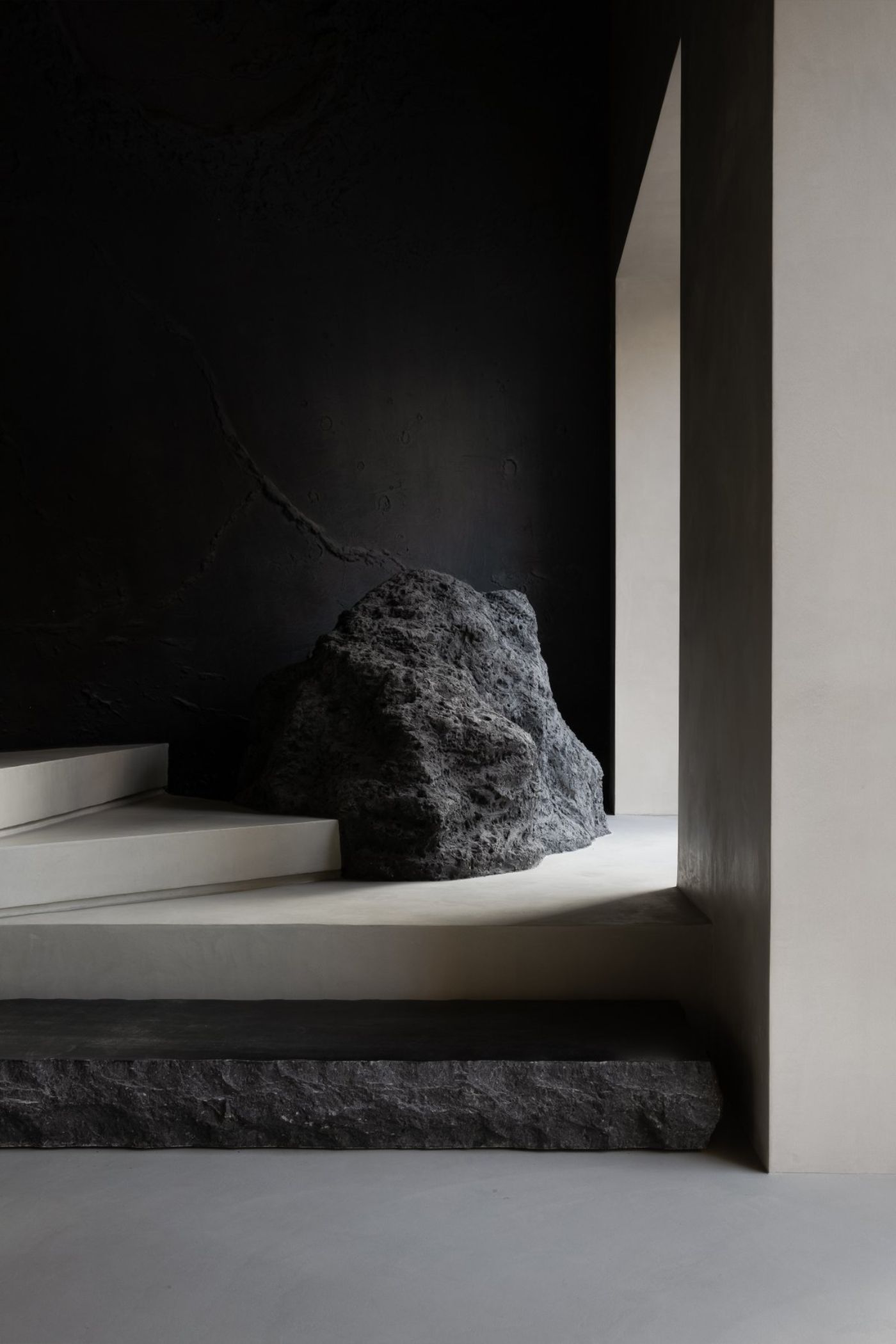 Novacolor Store by LICO Design — A recessed alcove frames an unfinished granite boulder positioned beneath a cantilevered stair.