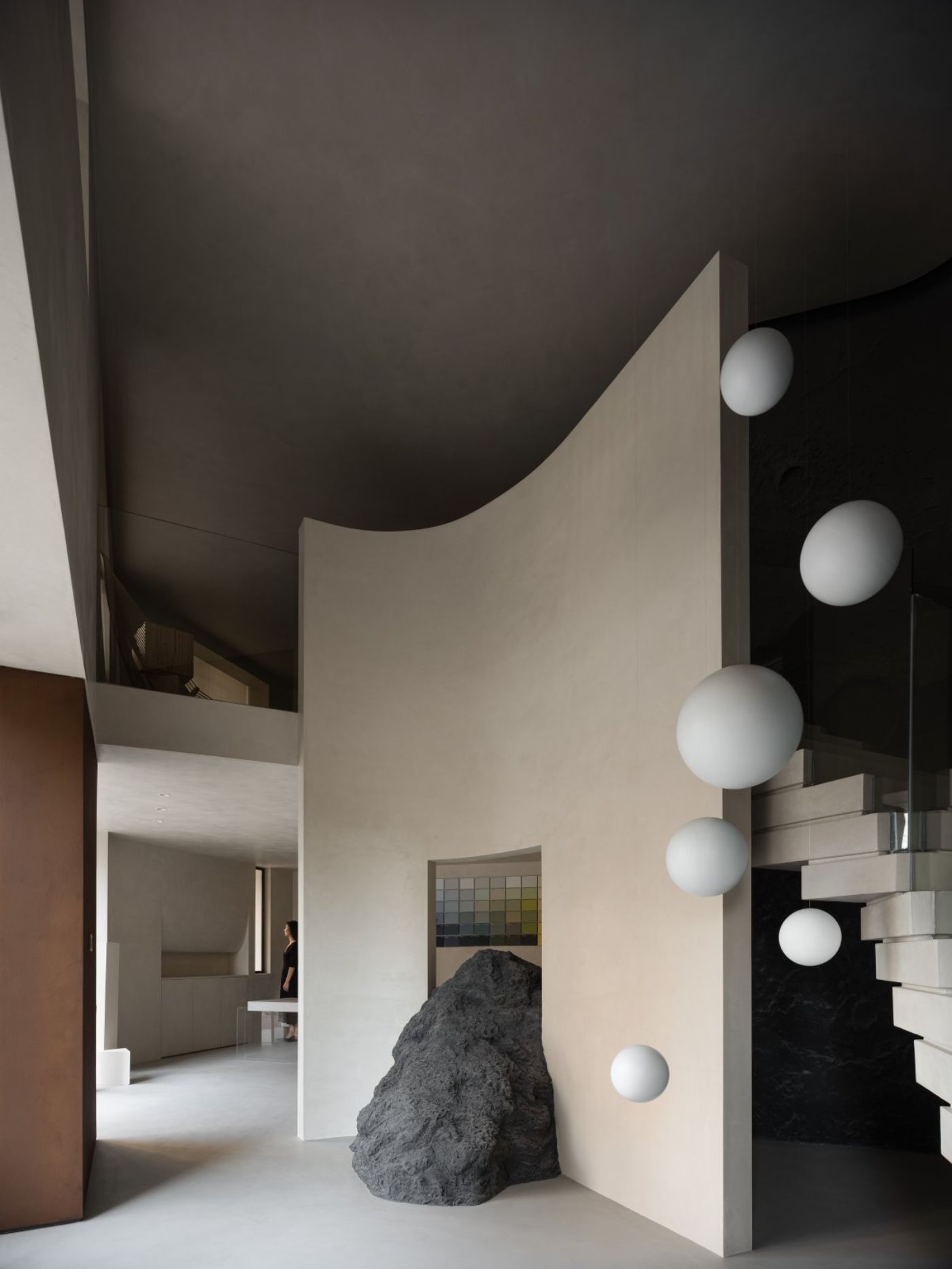 Novacolor Store by LICO Design — The Novacolor Store interior features a sculptural composition anchored by a large unfinished stone boulder positioned beneath a curved plaster wall.