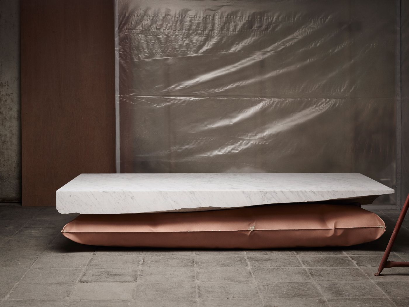 In Hale Wallpiece by Ben Storms — Ben Storms' inflated metal cushion is positioned horizontally against a terracotta wall panel, its surface rippling with deep creases and reflecting light...