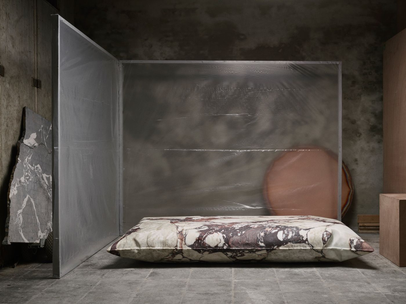 In Hale Wallpiece by Ben Storms — A inflated copper sheet metal cushion leans against a terracotta-colored panel in a raw concrete interior.