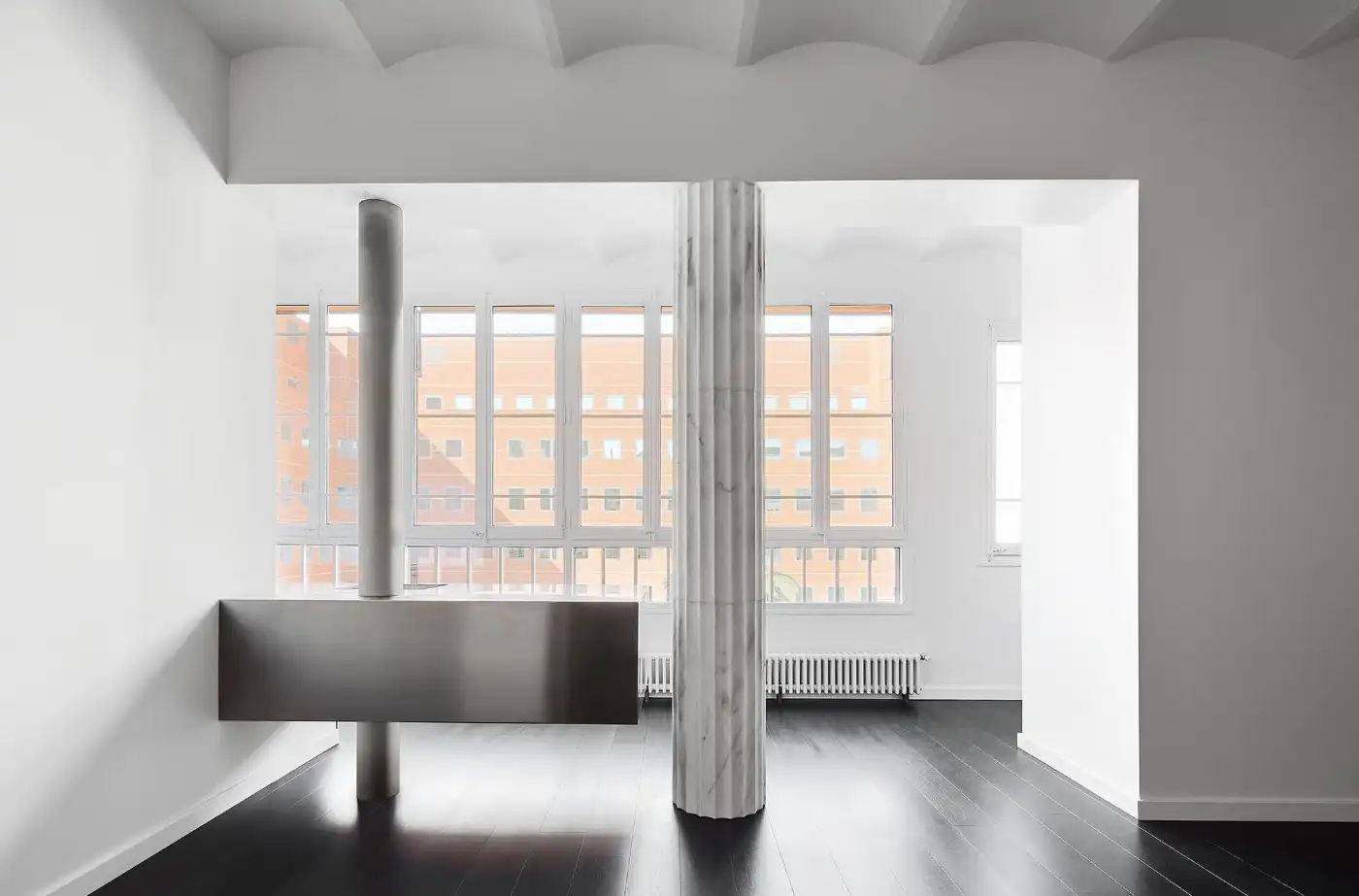 Flat in Eixample by Jaime Prous Architects — A double-height interior space divided by a sculptural support system comprising a fluted marble column and stainless-steel cylindrical pillar rising from a...