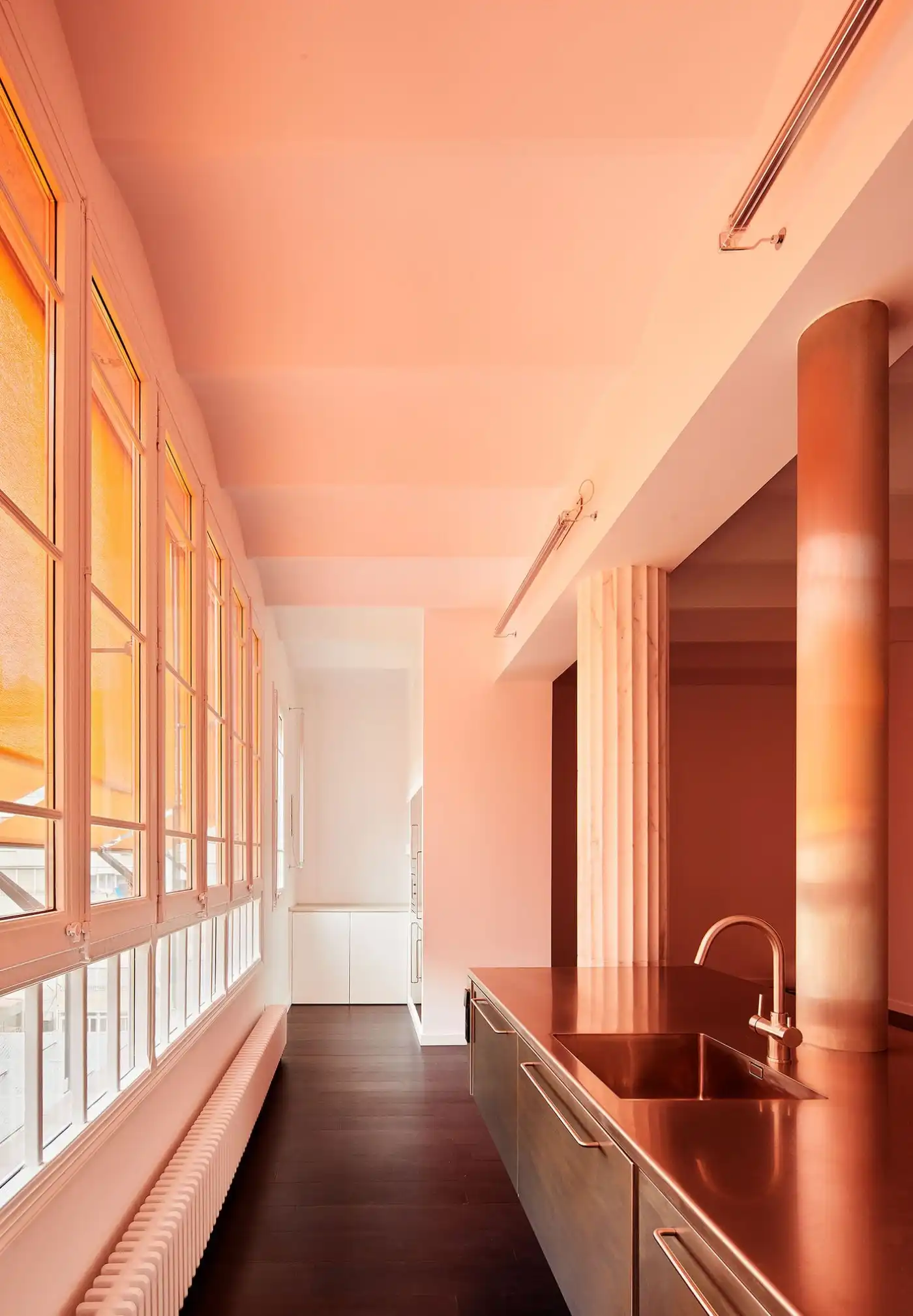 Flat in Eixample by Jaime Prous Architects — A galley kitchen bathed in golden-hour light streaming through multi-pane steel-framed windows along the left wall.