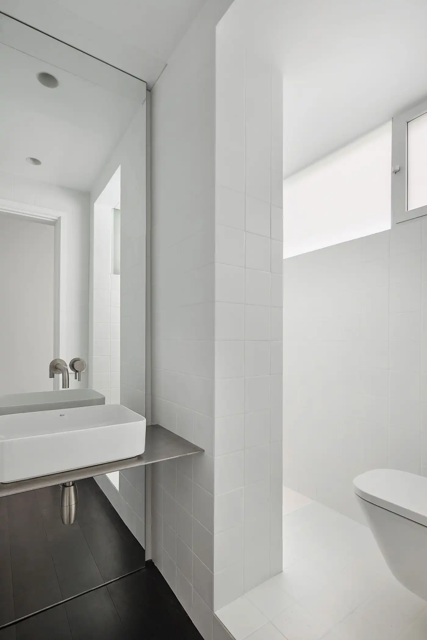 Flat in Eixample by Jaime Prous Architects — Bathroom interior with a white ceramic vessel sink cantilevered from a stainless-steel cylindrical support, positioned against white subway tile walls.