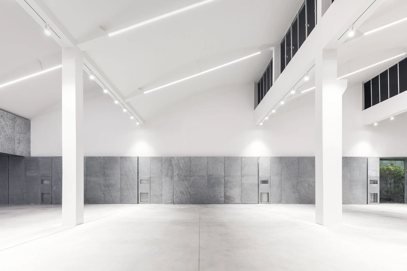 Spazio Maiocchi in Milan — A large gallery volume with exposed structural columns and suspended linear ceiling elements that cast sharp shadows across the white soffit.