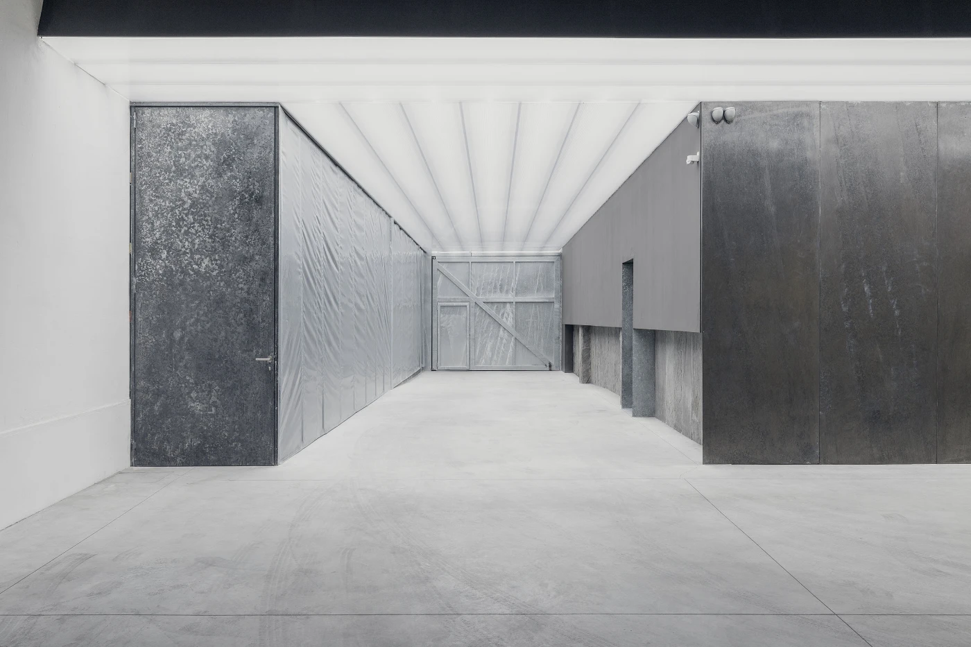 Spazio Maiocchi in Milan — A corridor within the former industrial building features a radial ceiling geometry of linear white elements that converge toward a distant glazed...