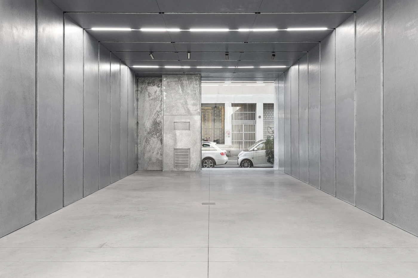 Spazio Maiocchi in Milan — A double-height corridor in polished concrete frames the street beyond through glazed partitions.