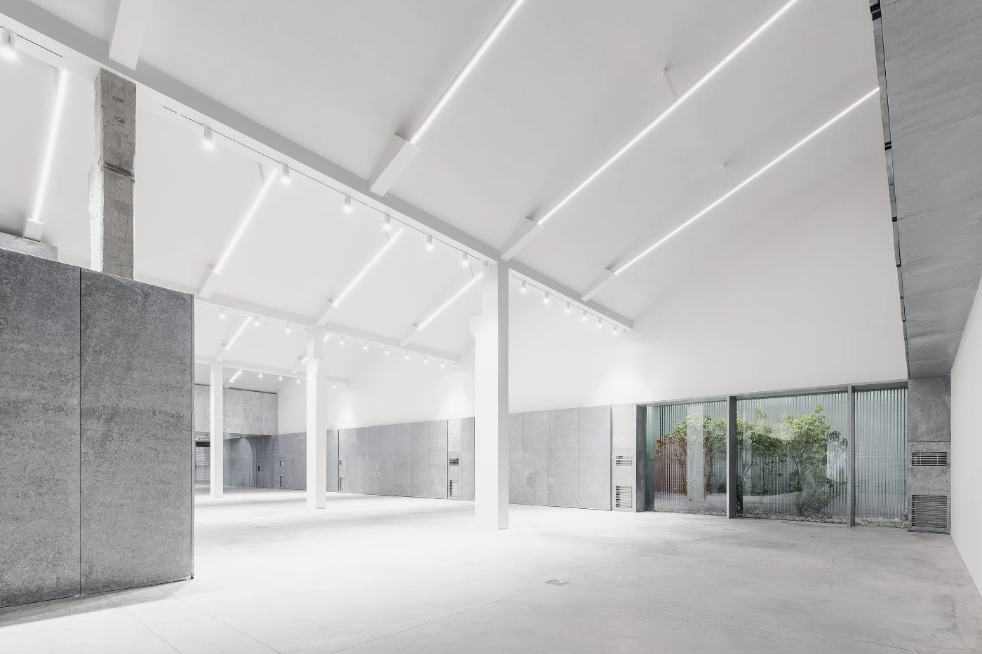 Spazio Maiocchi in Milan — A vast exhibition hall flooded with cool white light from linear ceiling elements that cast sharp geometric shadows across the polished concrete floor.