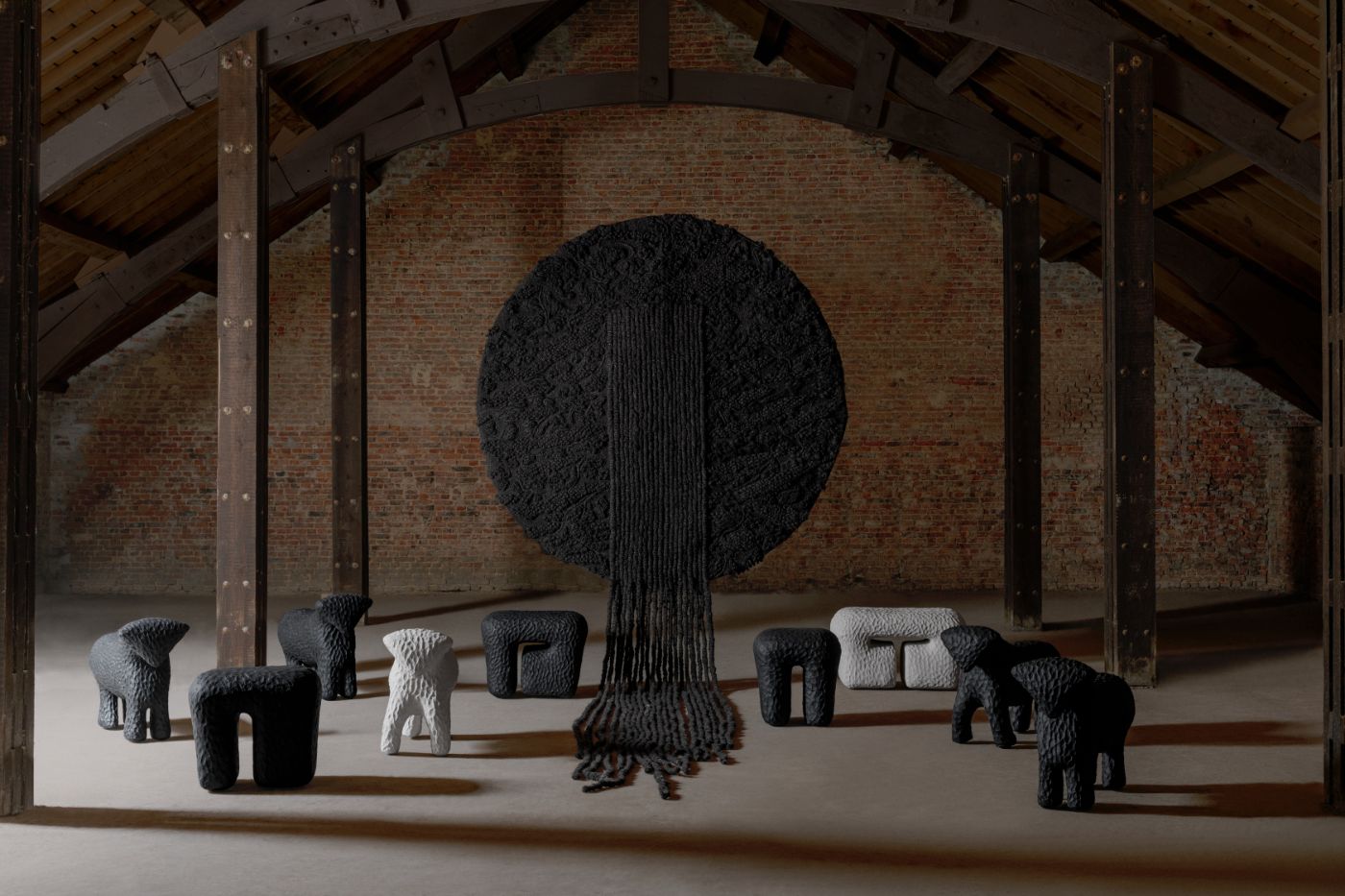 Limited collection by Victoria Yakusha — Hand-sculpted stools with textured, pitted surfaces arranged in spatial formation around a monumental wall-mounted tapestry.