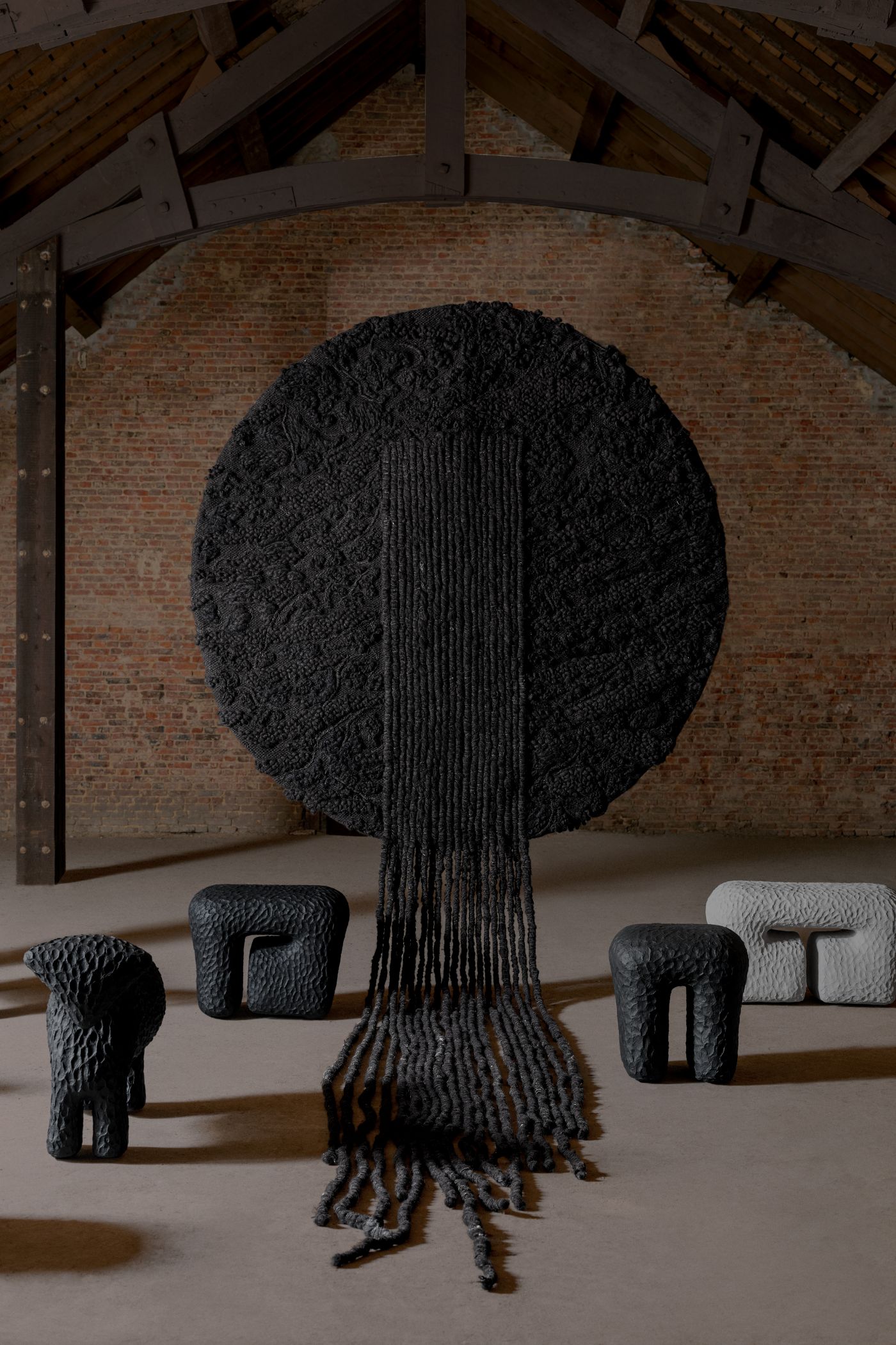 Limited collection by Victoria Yakusha — A hand-woven textile wall installation dominates the composition, depicting a stylized tree form rendered in charcoal-toned fibers.