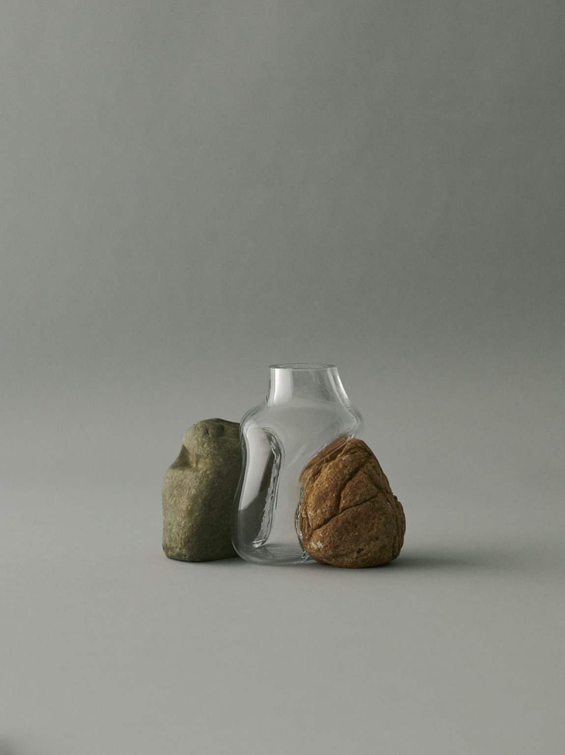 Vase Sculptures by Lætitia Jacquetton — A mouth-blown glass vessel with an asymmetrical, bulbous form cradles two weathered stones collected from natural settings.