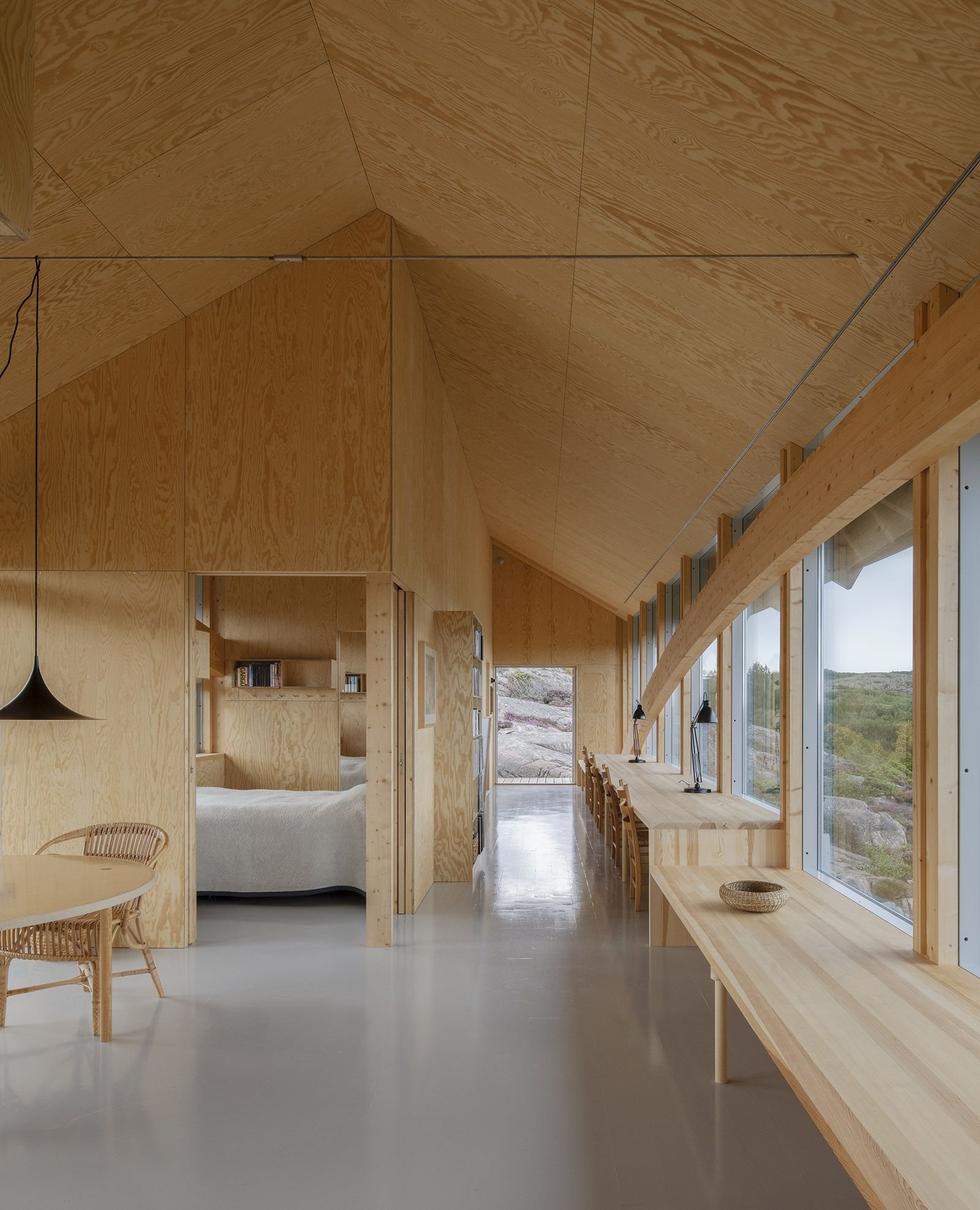 House Hamburgö by Manthey Kula — Interior view of the 29-meter timber arch bridge revealing the continuous glazing band framing landscape vistas across glacial terrain.