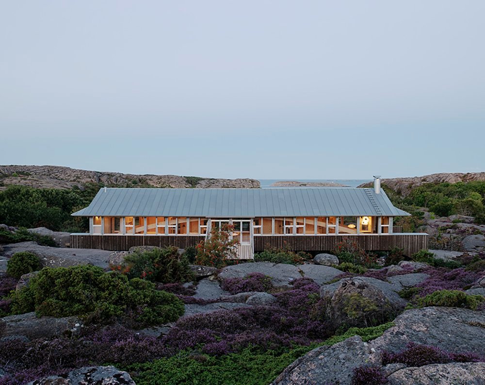 House Hamburgö by Manthey Kula — House Hamburgö spans 29 meters across glacial granite bedrock in Bohuslän, Sweden, its corrugated metal envelope patinated to warm grey rising on slender...