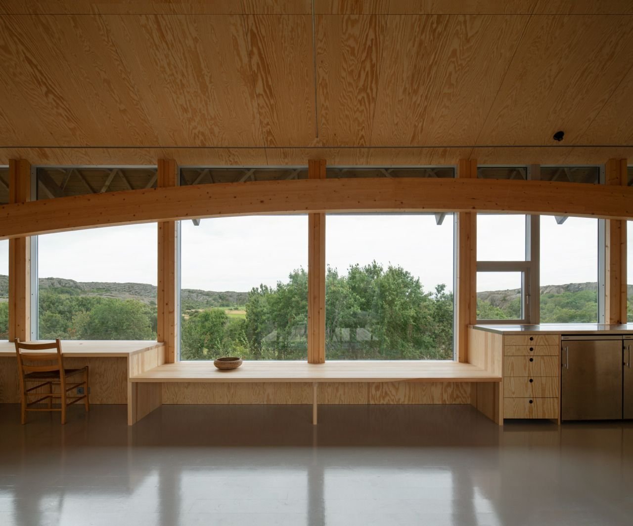 House Hamburgö by Manthey Kula — A timber-framed interior spans horizontally across glacial bedrock, its load-bearing laminated arches visible beneath the envelope.