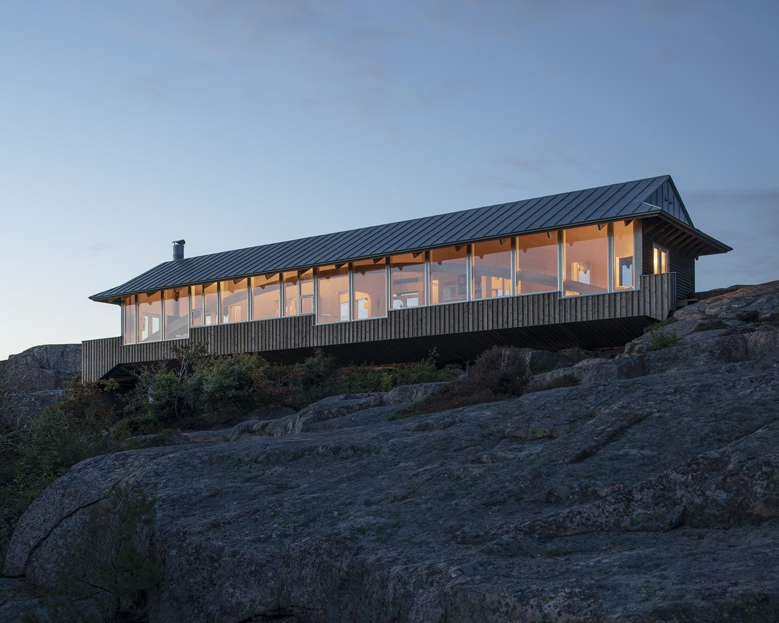 House Hamburgö by Manthey Kula — House Hamburgö appears as a linear pavilion suspended across glacial bedrock, its 29-meter span supported by two laminated timber arches that distribute...