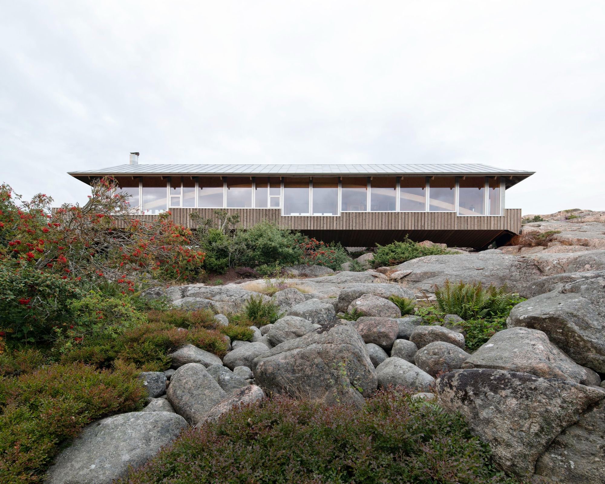 House Hamburgö by Manthey Kula — House Hamburgö spans 29 meters across glacial boulders via two laminated timber arches, its corrugated metal cladding displaying a warm grey patina.