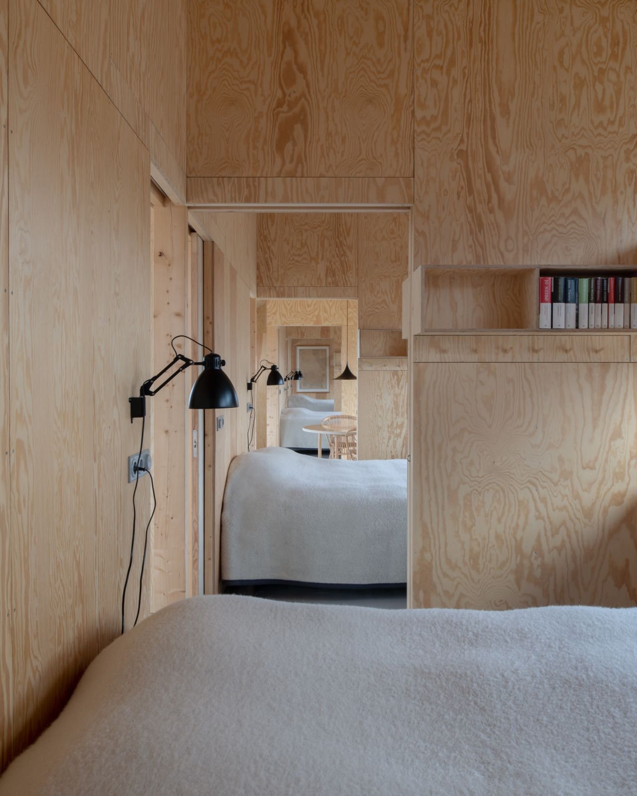 House Hamburgö by Manthey Kula — Interior view of the timber-lined bridge house, showing continuous wood-clad walls in natural plywood that frame the spatial progression.