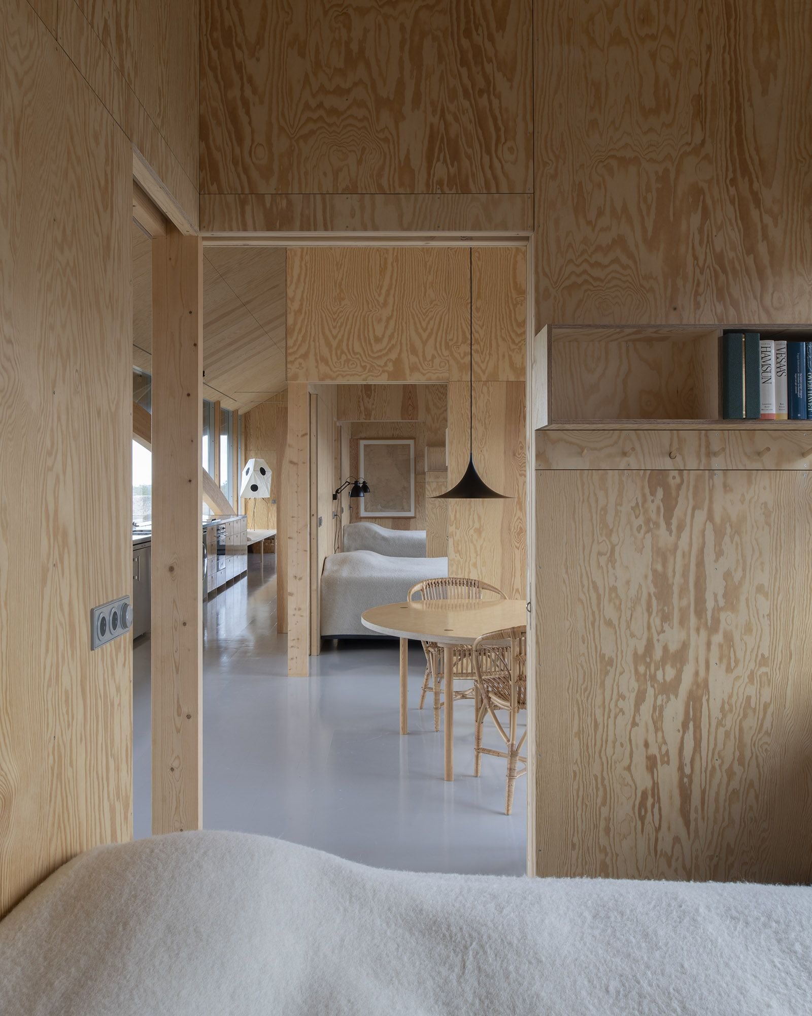House Hamburgö by Manthey Kula — Interior passage framing successive spatial zones through plywood walls and open thresholds.