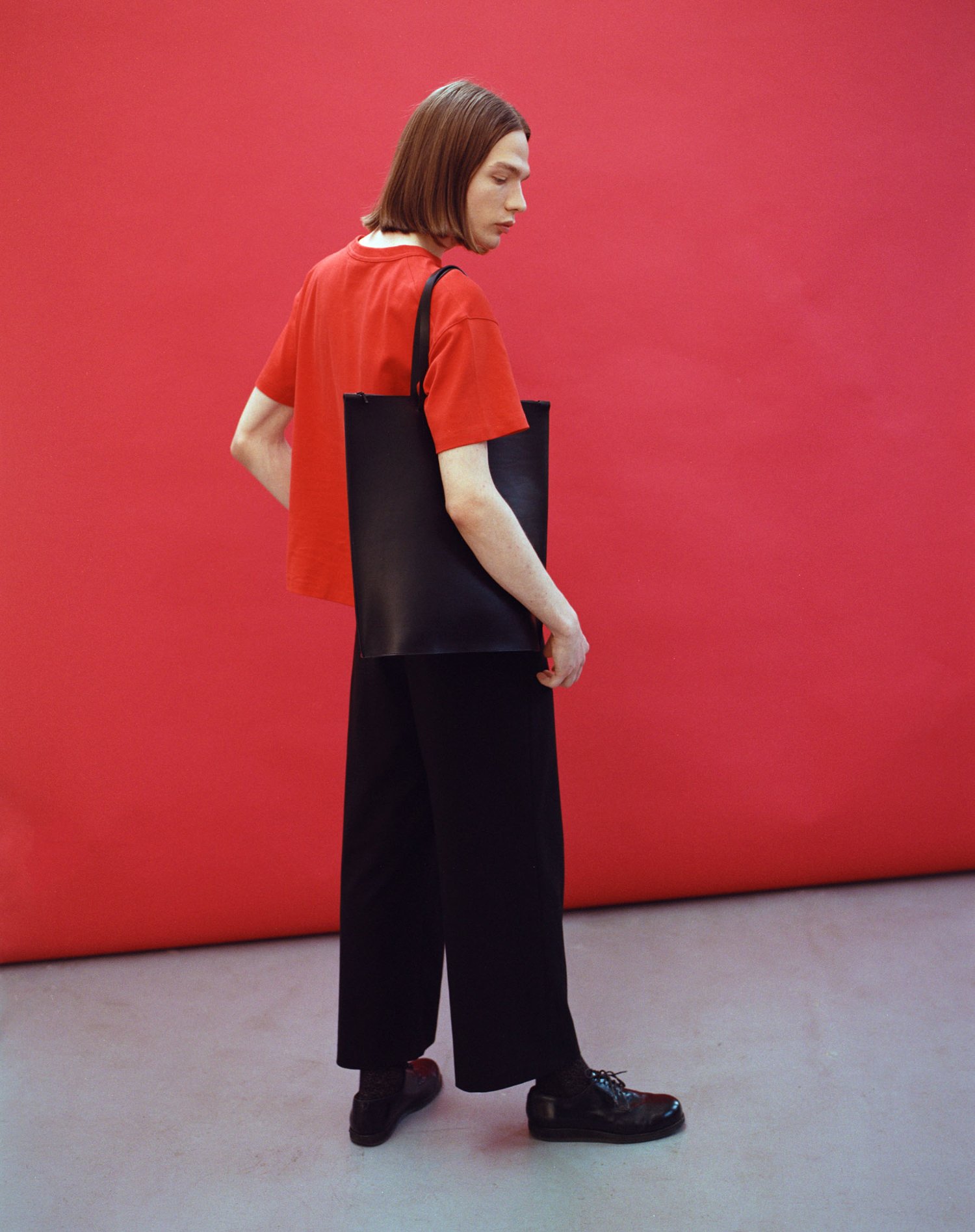 Yenisei by Thisispaper Studio — A figure in profile wears a black leather tote bag with minimal hardware against a vivid red wall.