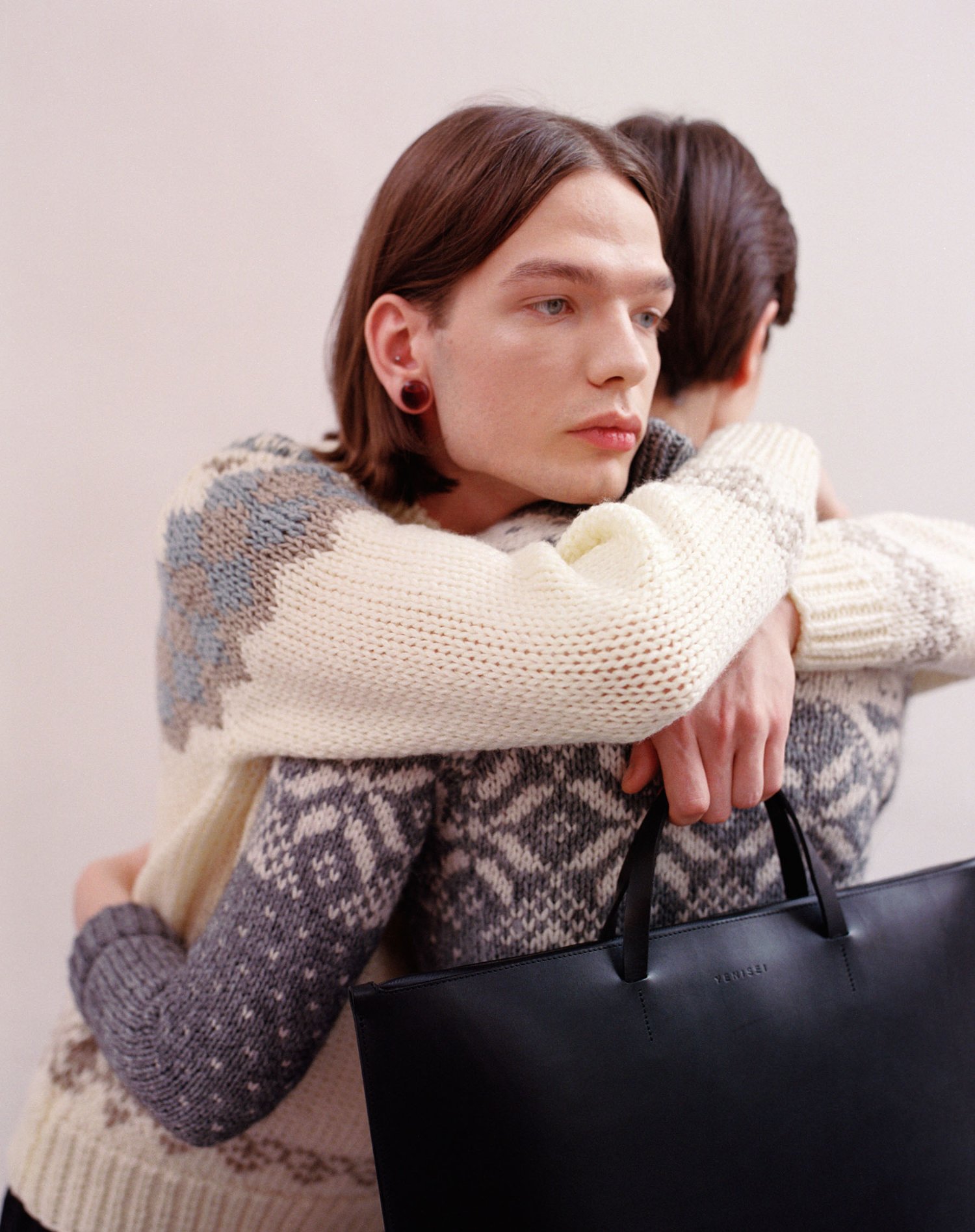 Yenisei by Thisispaper Studio — Product photograph featuring a black leather tote bag held by a figure wearing a patterned wool cardigan in grey and cream tones.