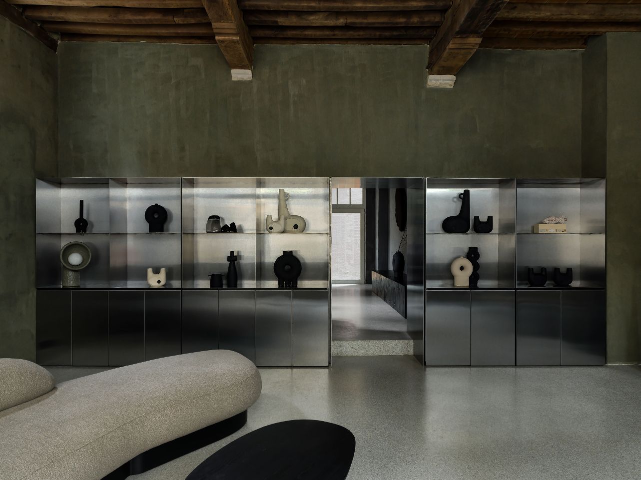 Faina Gallery by Yakusha Studio — A 500-year-old Antwerp building's interior gallery space features a continuous steel-framed vitrine system spanning the rear wall, displaying black ceramic...