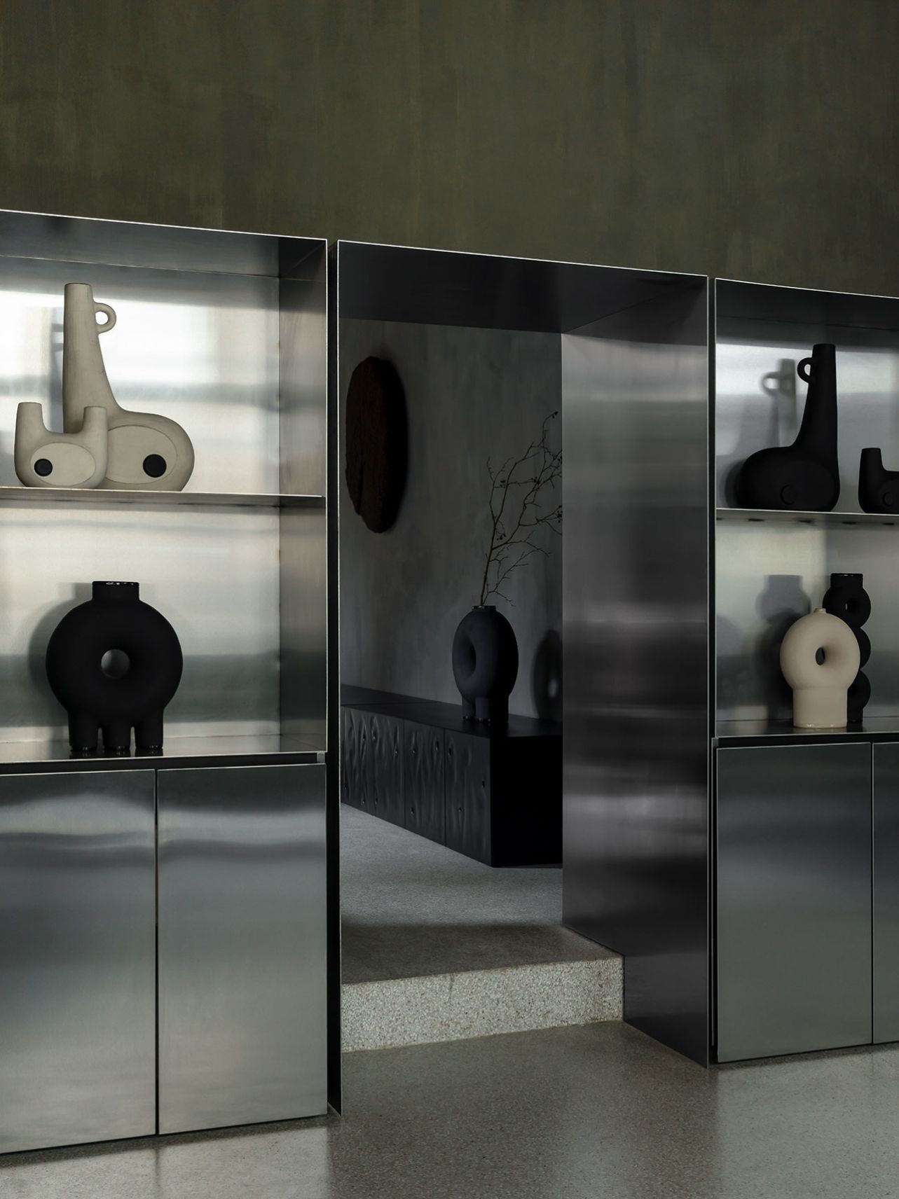 Faina Gallery by Yakusha Studio — A glazed display cabinet frames three tiers of sculptural ceramic vessels in contrasting black and cream finishes.