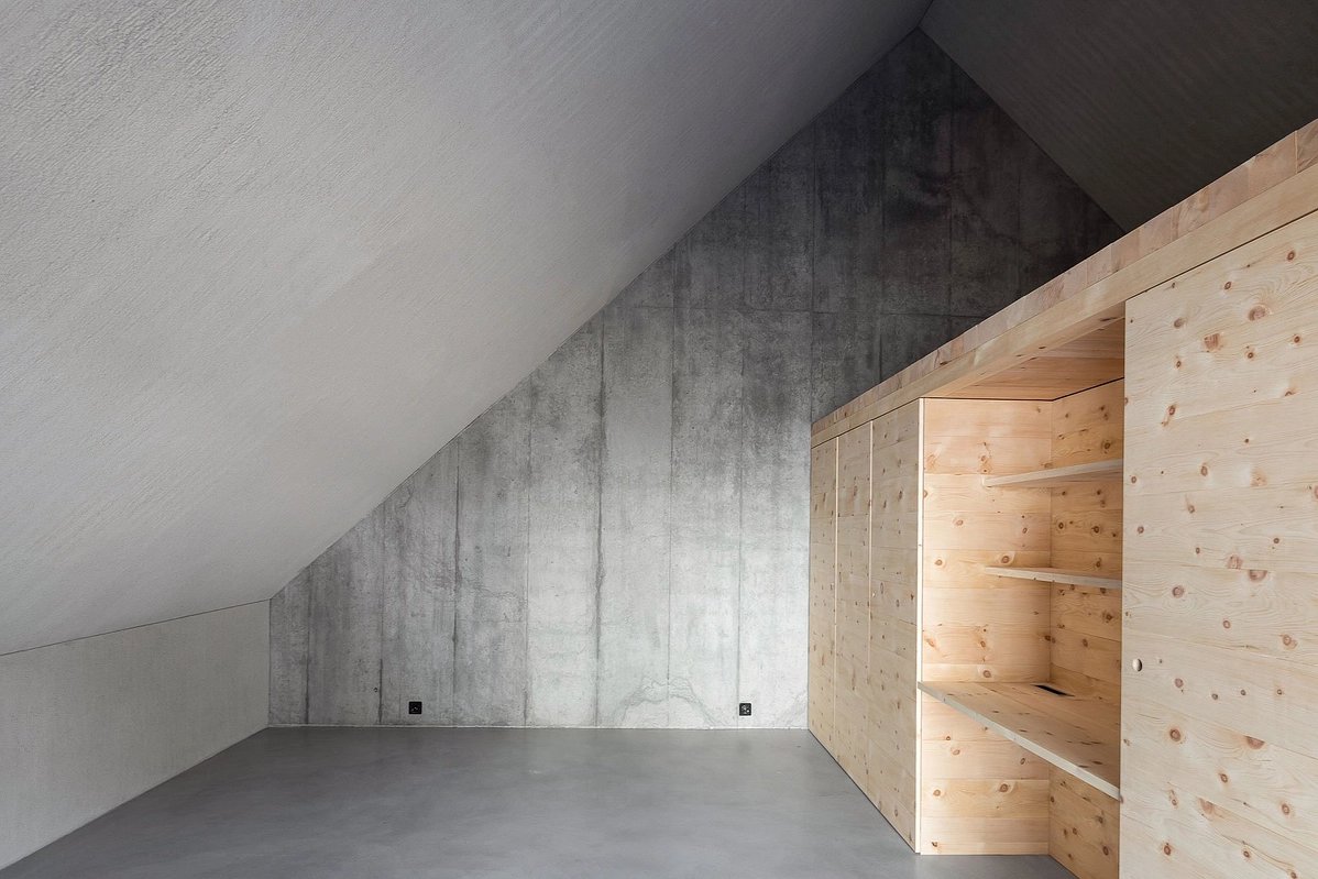 The Trin Cabin By Schneller Caminada Architects — Interior view of the Trin Cabin's upper floor, revealing the material contrast between the concrete structural wall and the pine storage cabinetry.