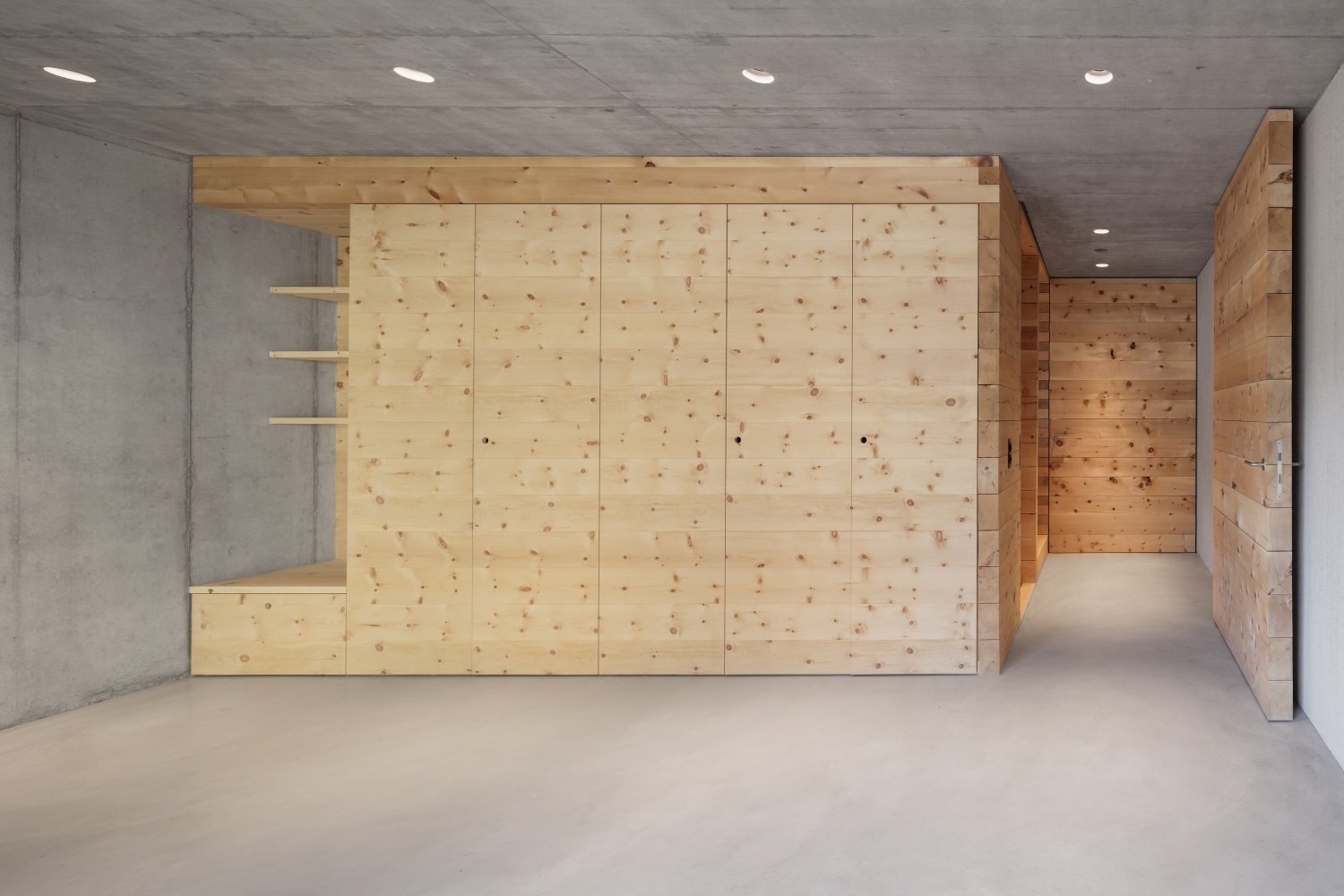 The Trin Cabin By Schneller Caminada Architects — Interior view of a three-story timber-clad structure under construction, featuring board-formed pine paneling with visible knots across five vertical sections.