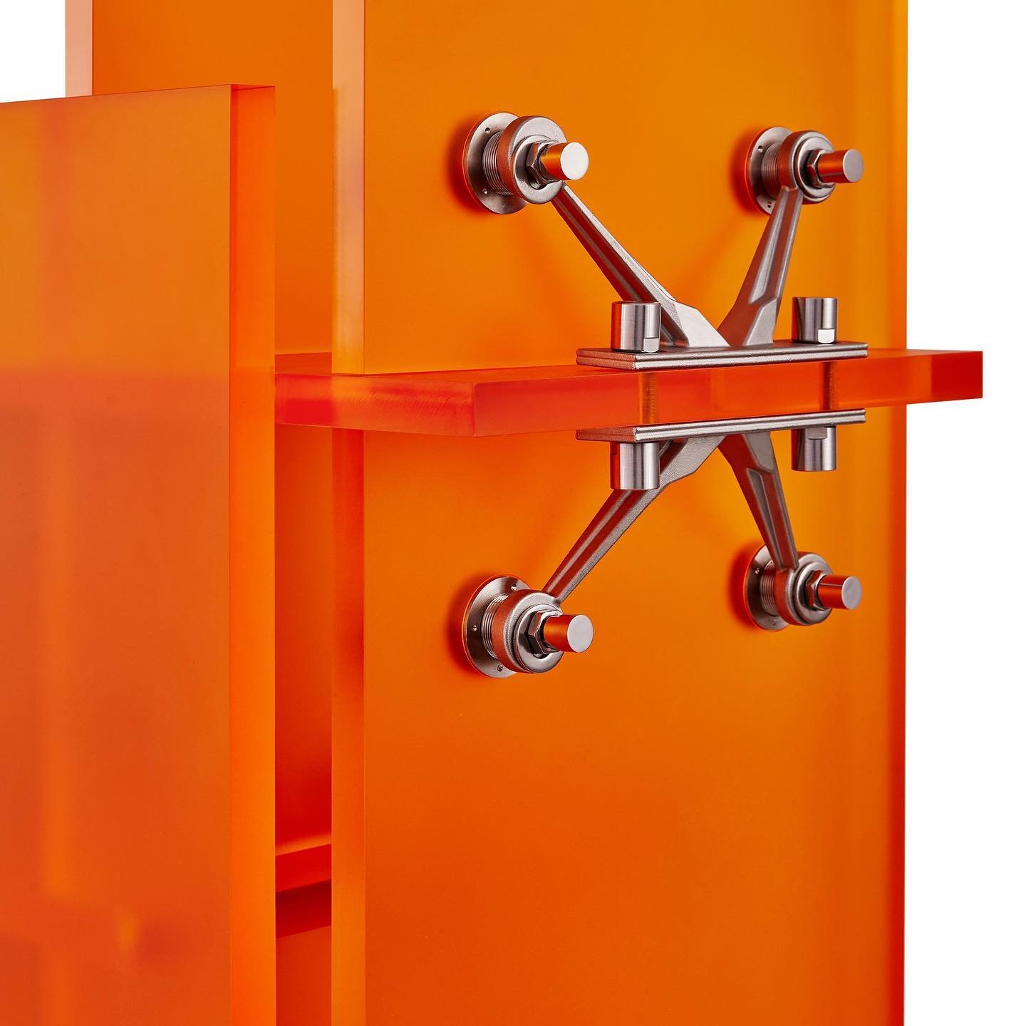 Mixed Public-Private Boundary collection by Cometabolism Studio — Cometabolism Studio's furniture object mounted on a vivid orange panel wall, featuring four chrome-finished mechanical connectors anchoring dark red steel...