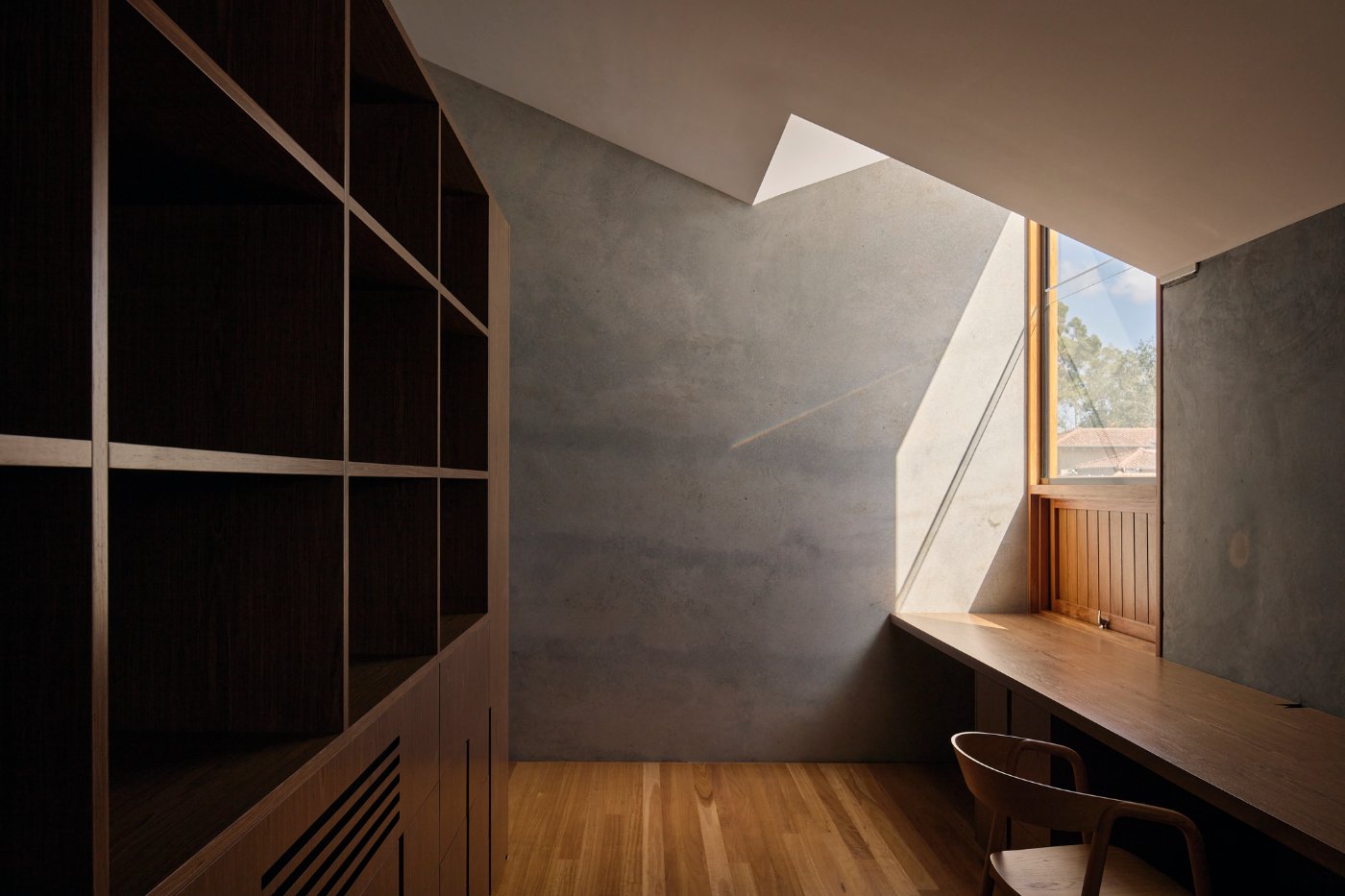Chelmer River House by Furminger by Christopher Furminger — A timber desk positioned beneath an angular skylight opening, flooded with natural light that cuts a geometric shadow across the concrete wall.
