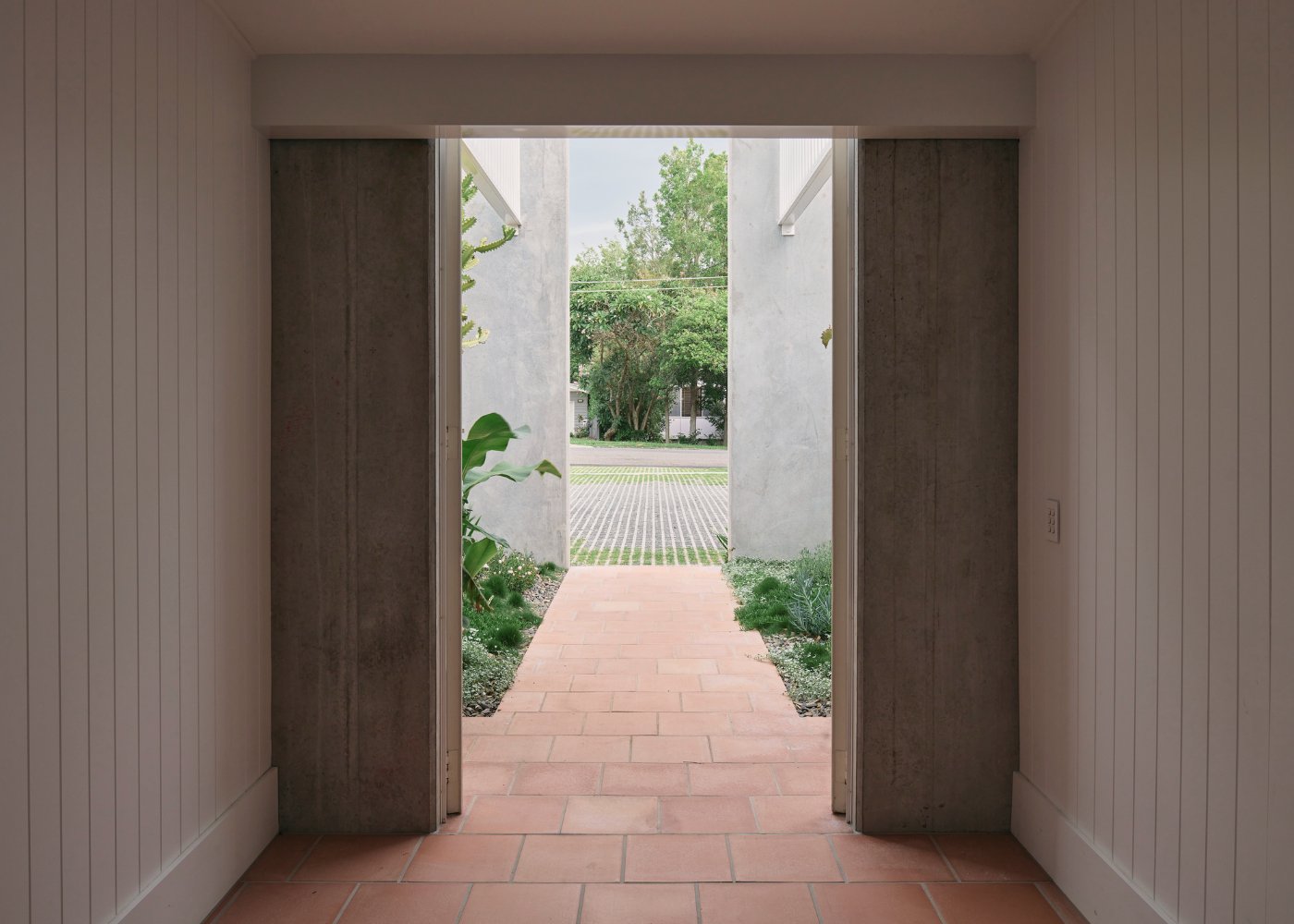 Chelmer River House by Furminger by Christopher Furminger — A passage framed by two monolithic tilt-up concrete panel walls with minimal fenestration, their dark rendered surfaces creating a compressed vertical corridor.