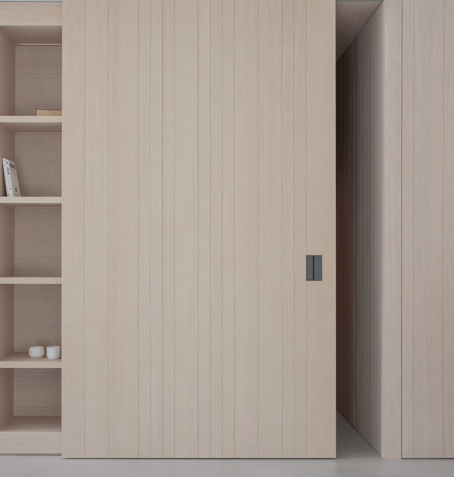 BI Apartment by Francesc Rifé Studio — A minimalist interior corner showcasing vertical oak wood slats in natural finish, punctuated by a single recessed pull handle in dark metal.