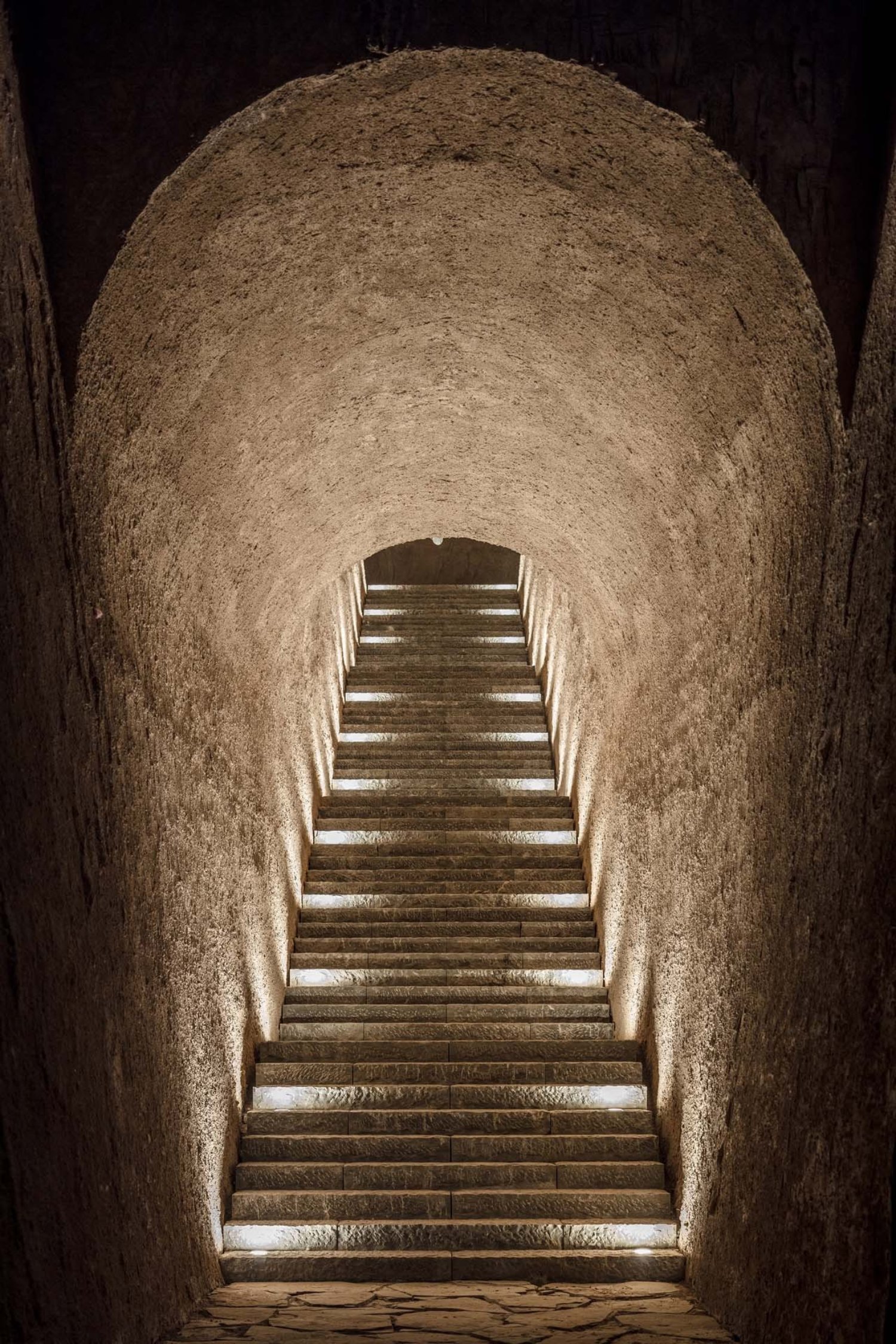 Holy Fire Lit Place in China by URBANUS — A monolithic earthen passage frames a monumental staircase ascending toward natural light.