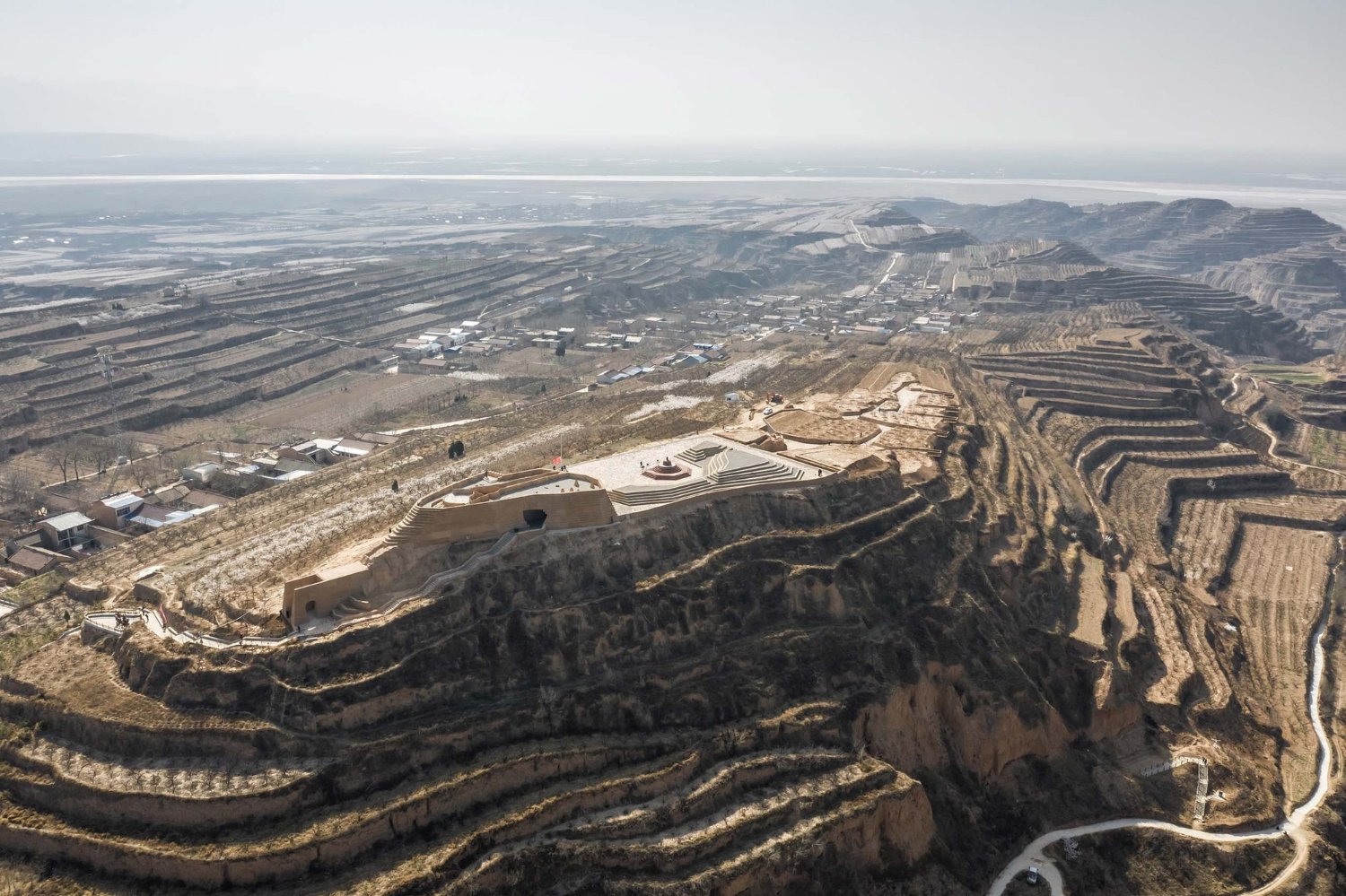 Holy Fire Lit Place in China by URBANUS — Aerial photograph revealing the Holy Fire Lit Place museum carved into earthen hillside above the Yellow River floodplain.