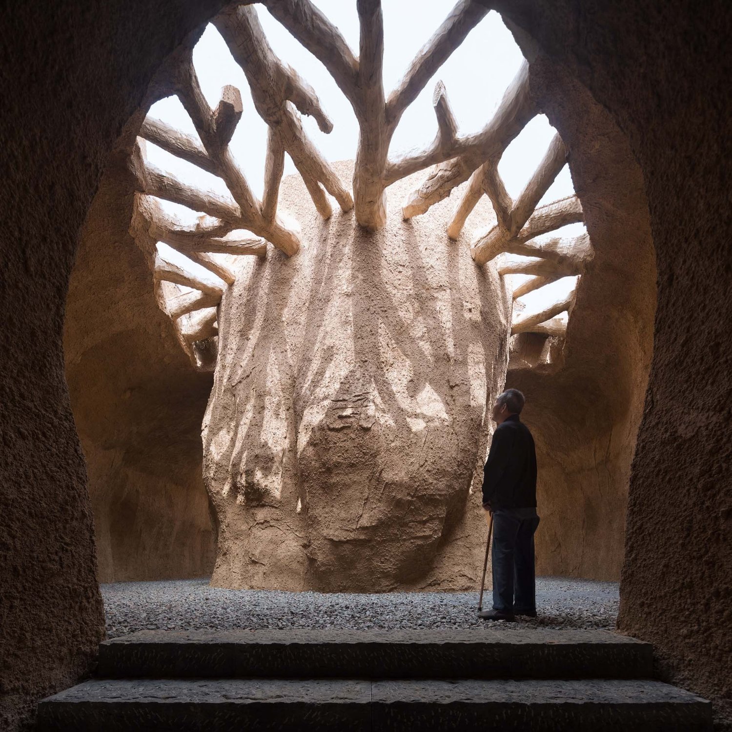 Holy Fire Lit Place in China by URBANUS — A monolithic earthen mass carved into a towering tree-form dominates this interior chamber at the Xihoudu archaeological museum.